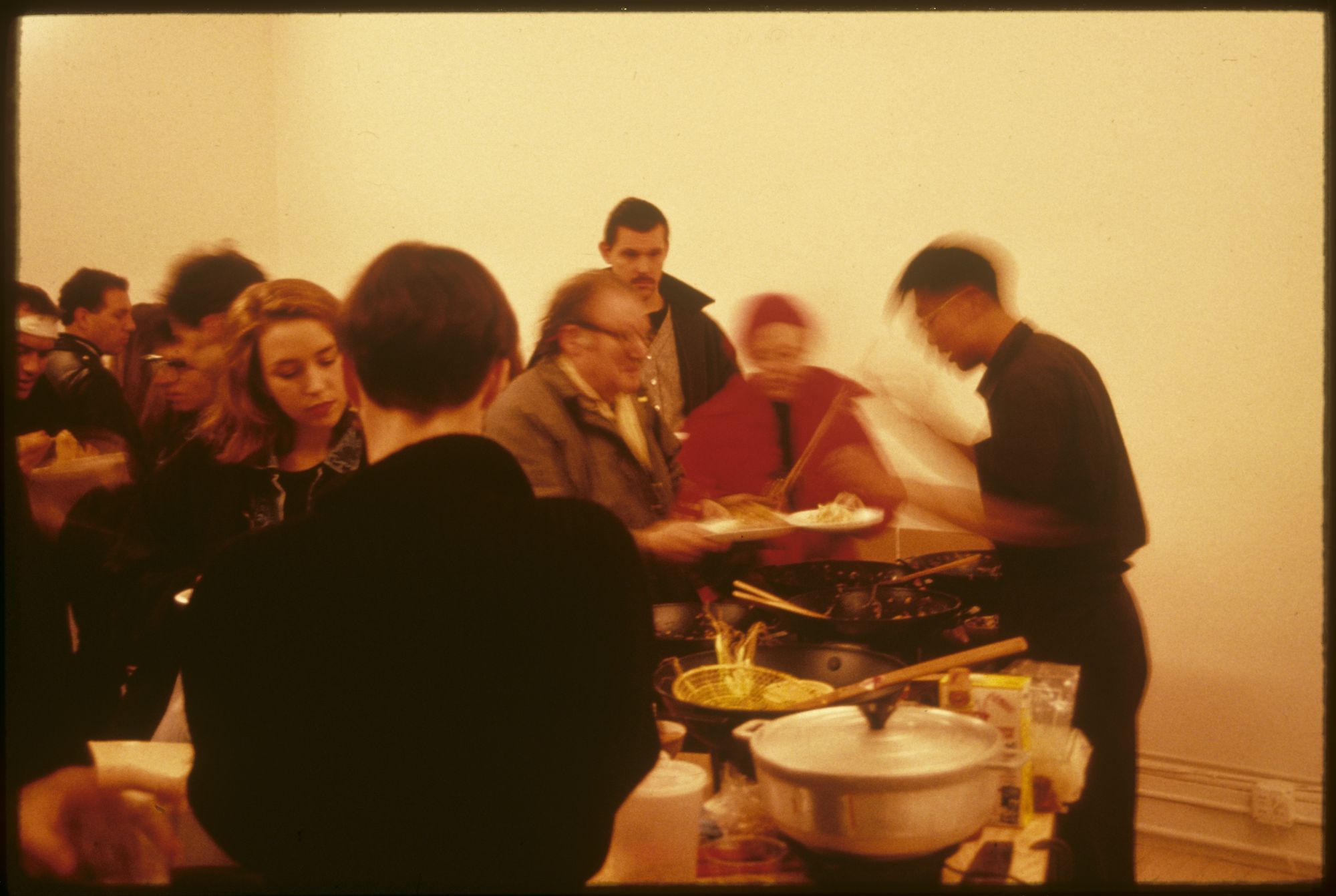An image of a group of people standing next to an artist who's cooking phad thai.