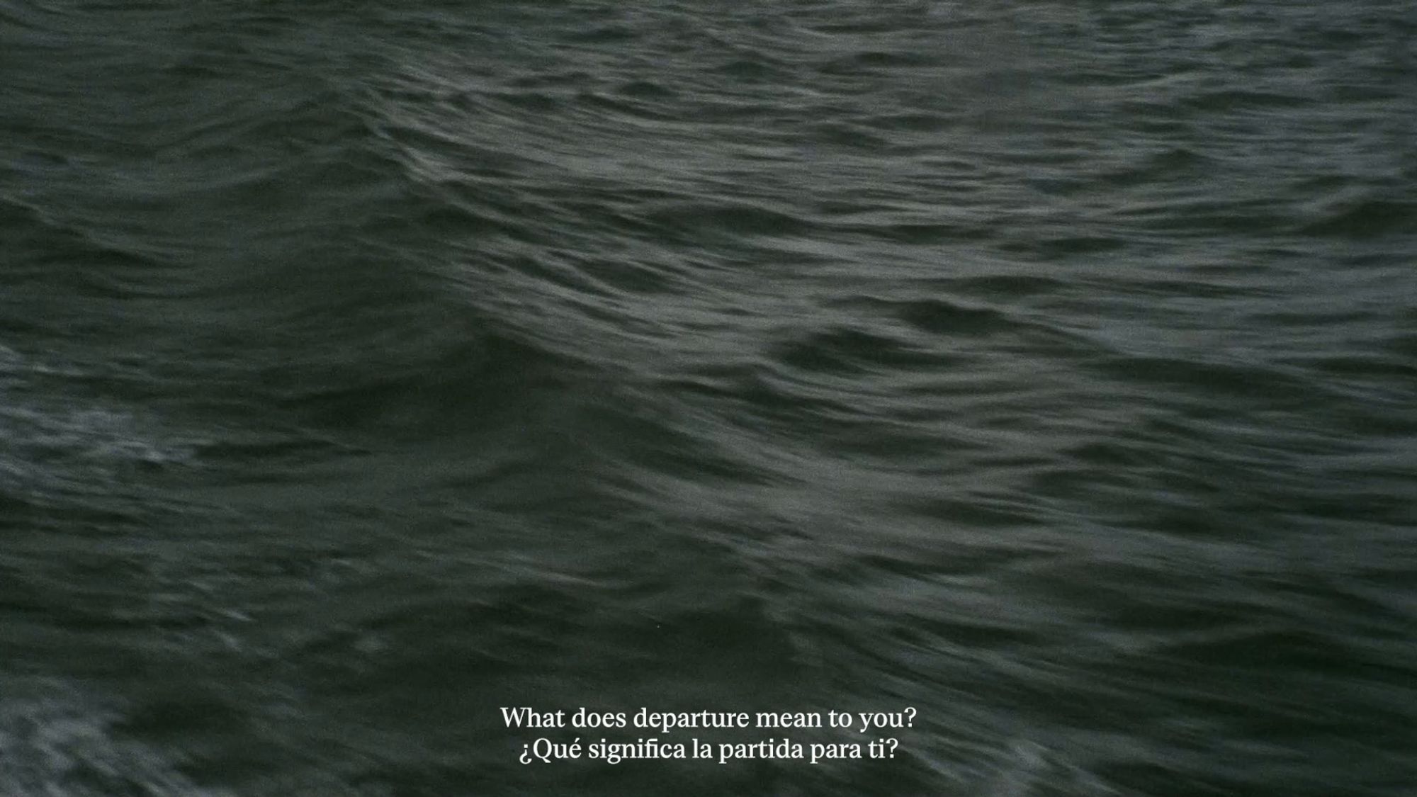 A shot of the ocean, with a subtitle below that reads: "What does departure mean to you?" in English and Spanish