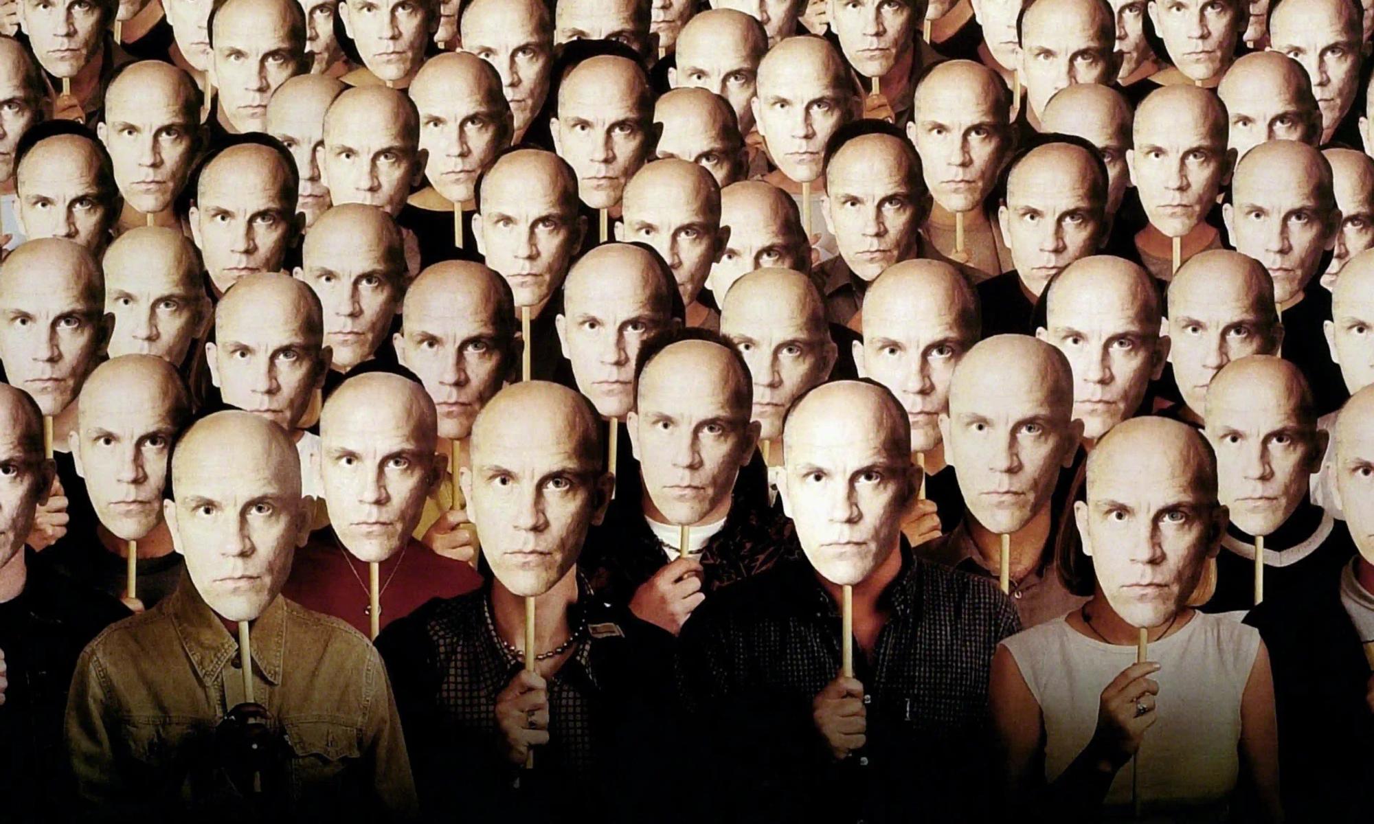 A crowd of figures, with different clothes and bodies, all hold up uniform masks with the face of John Malkovich staring seriously forward.