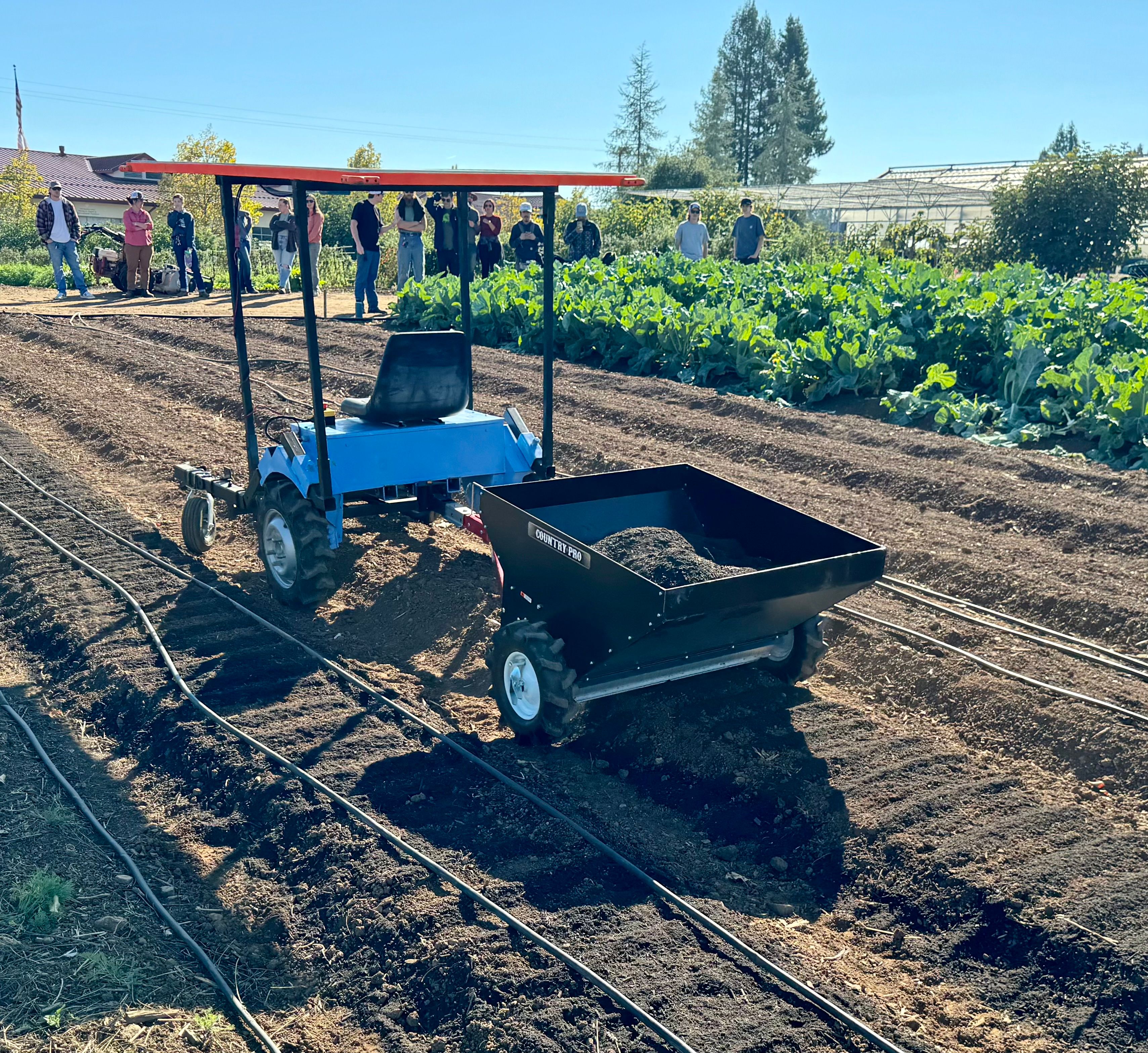 The e2T, a small blue electric tractor tows compost in a field. 