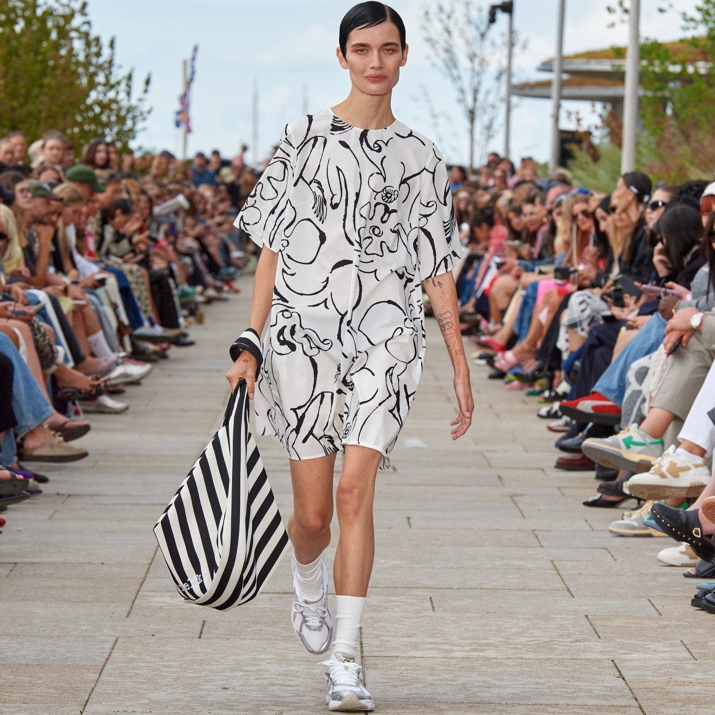 Model walking on the catwalk of the fashion show dressed in a black and white Blossoming Baluns dress.