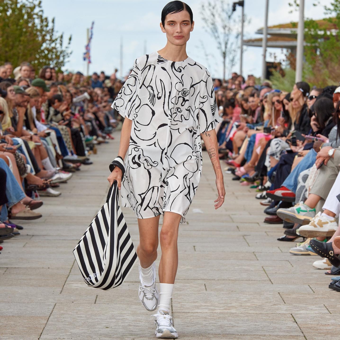 Model walking on the catwalk of the fashion show dressed in a black and white Blossoming Baluns dress.