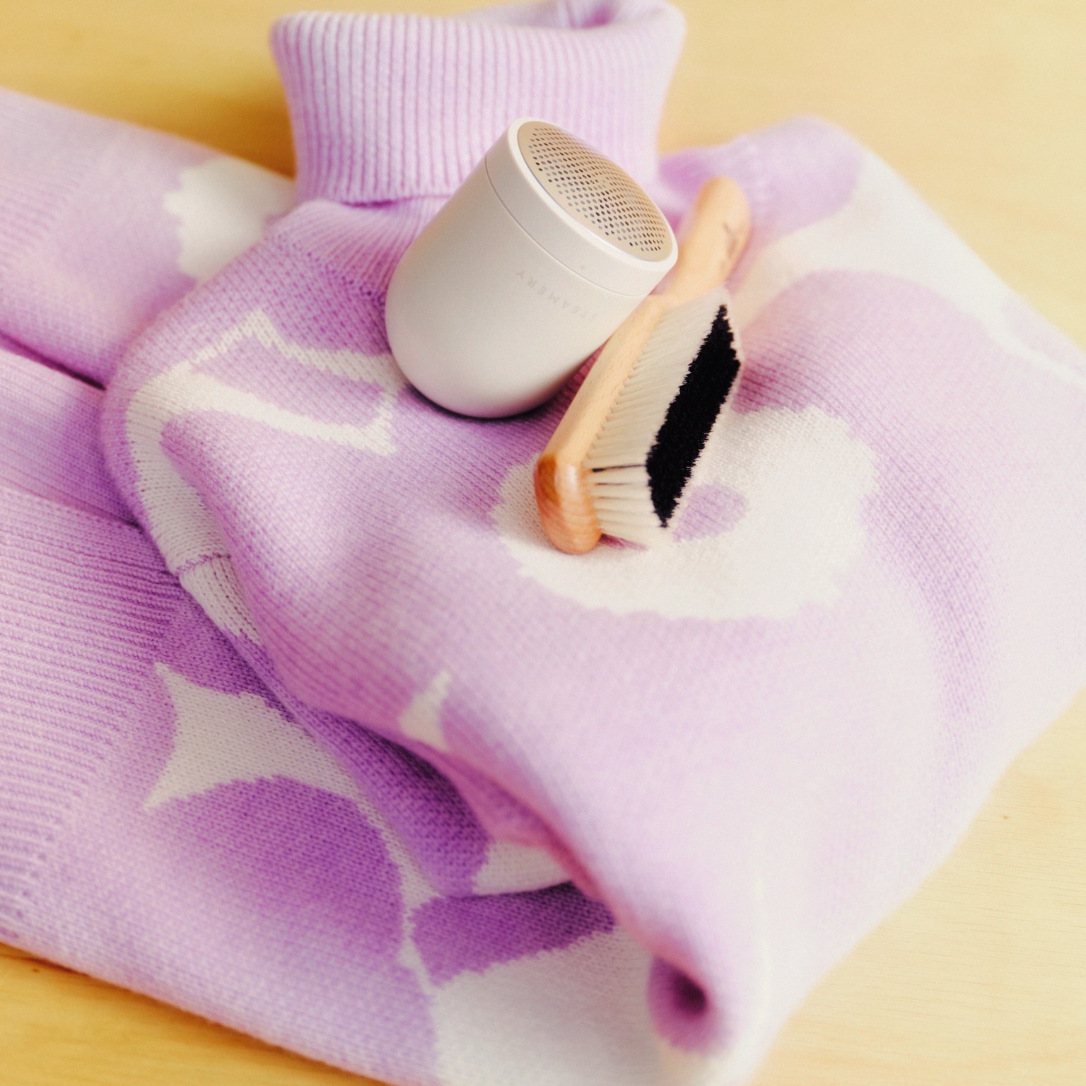 Neule Unikko-kuviolla ja neuleen hoitoon tarkoitetut tuotteet: Kent-vaateharja ja Steamery-nukkaleikkuri