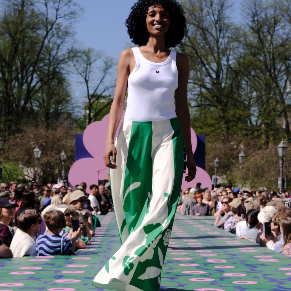 Malli pukeutuneena valkoiseen toppiin, jossa on musta Unikko-yksityiskohta ja vihreä-valkoiseen hameeseen