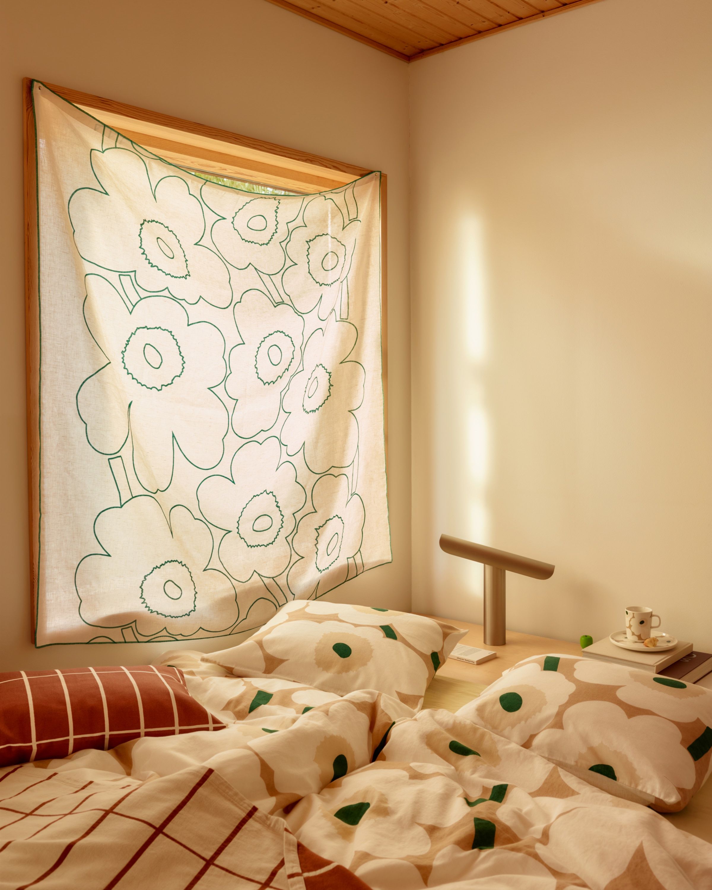 Bedlinen in Unikko print on a bed, and linen fabric in Piirto Unikko print hanging in front of a window.