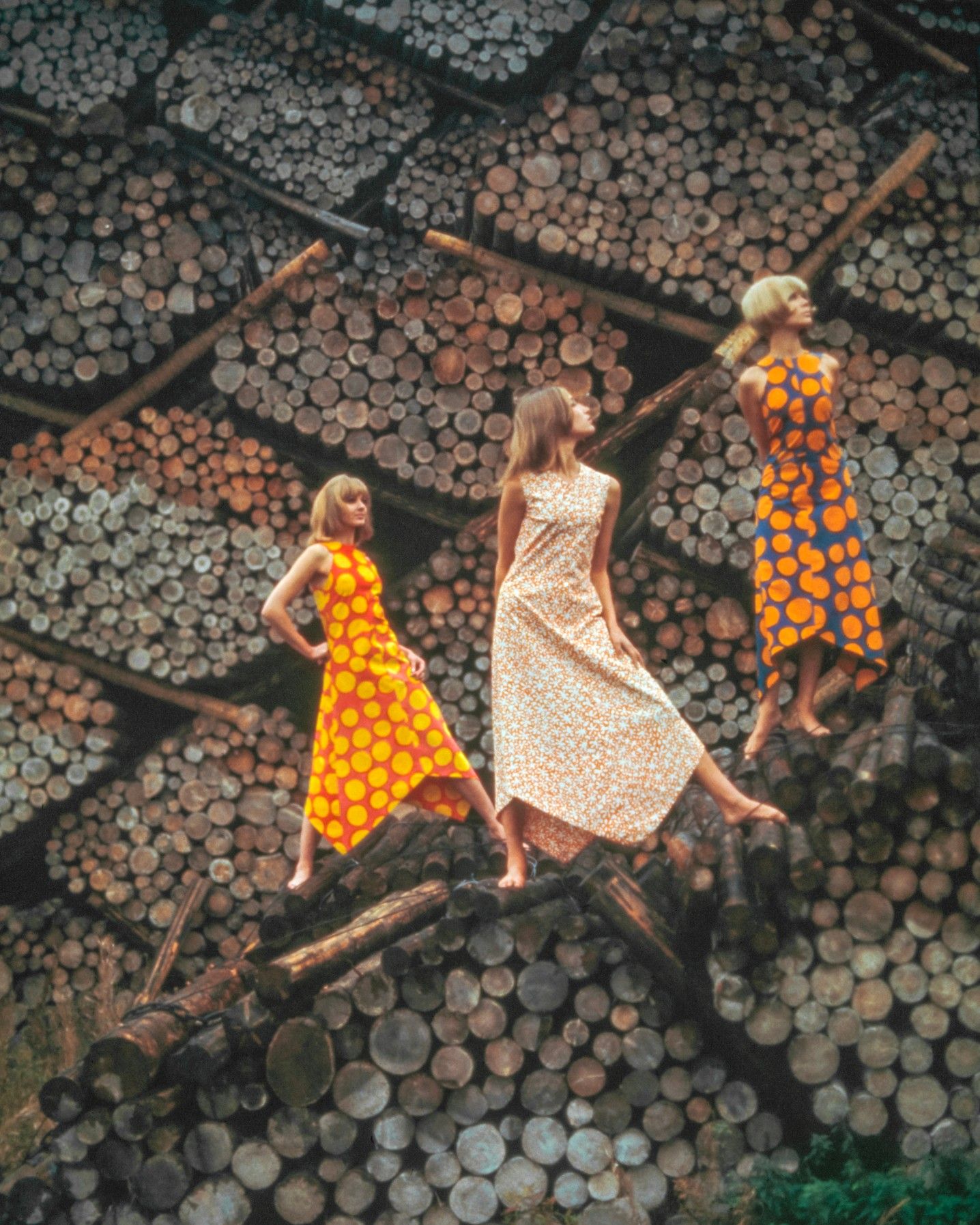 Photo by Tony Vaccaro of three models wearing Marimekko dresses and standing on top of a pile of logs.