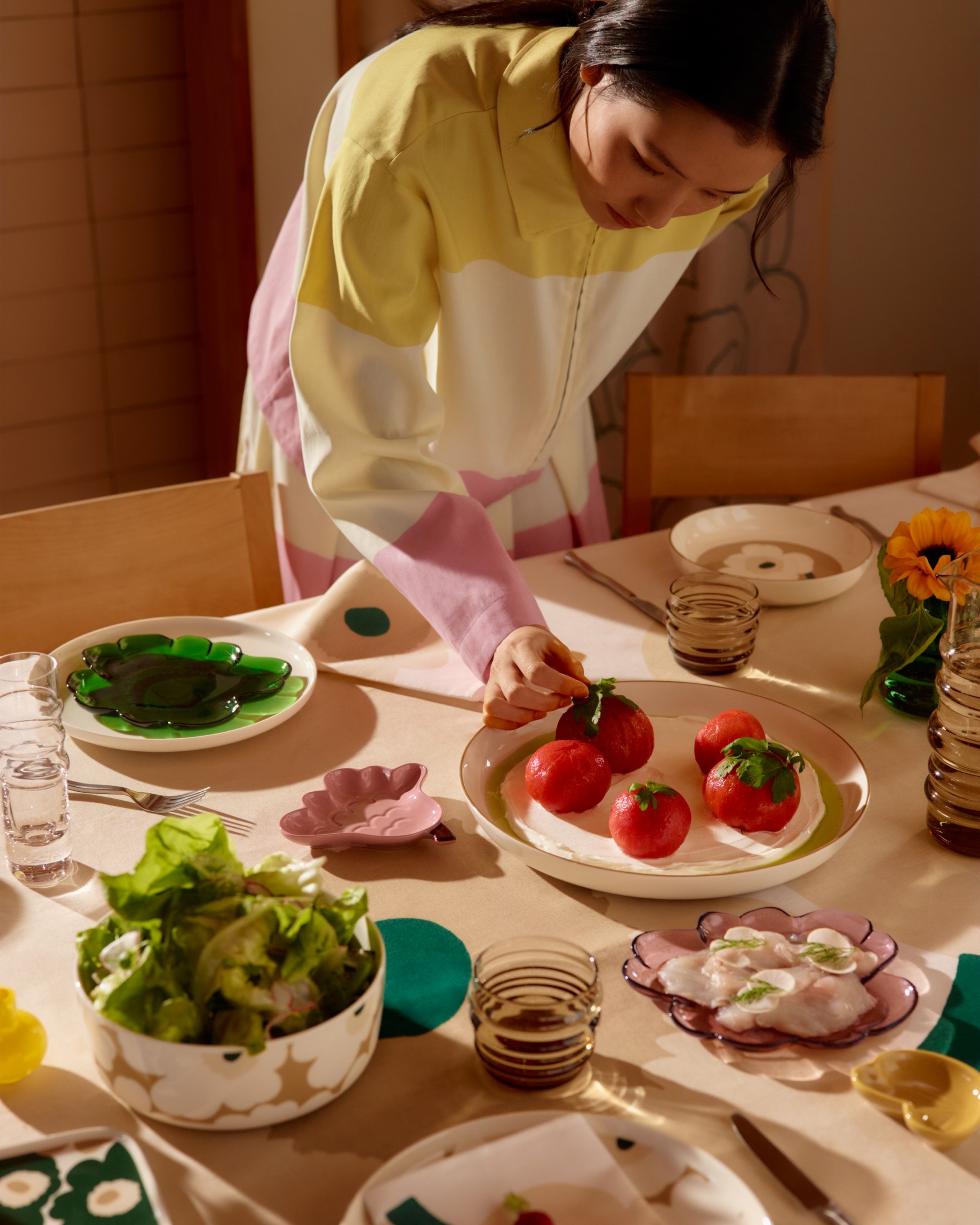 Marimekko ceramic tableware and glassware arranged on a table, with a model reaching to adjust served food.