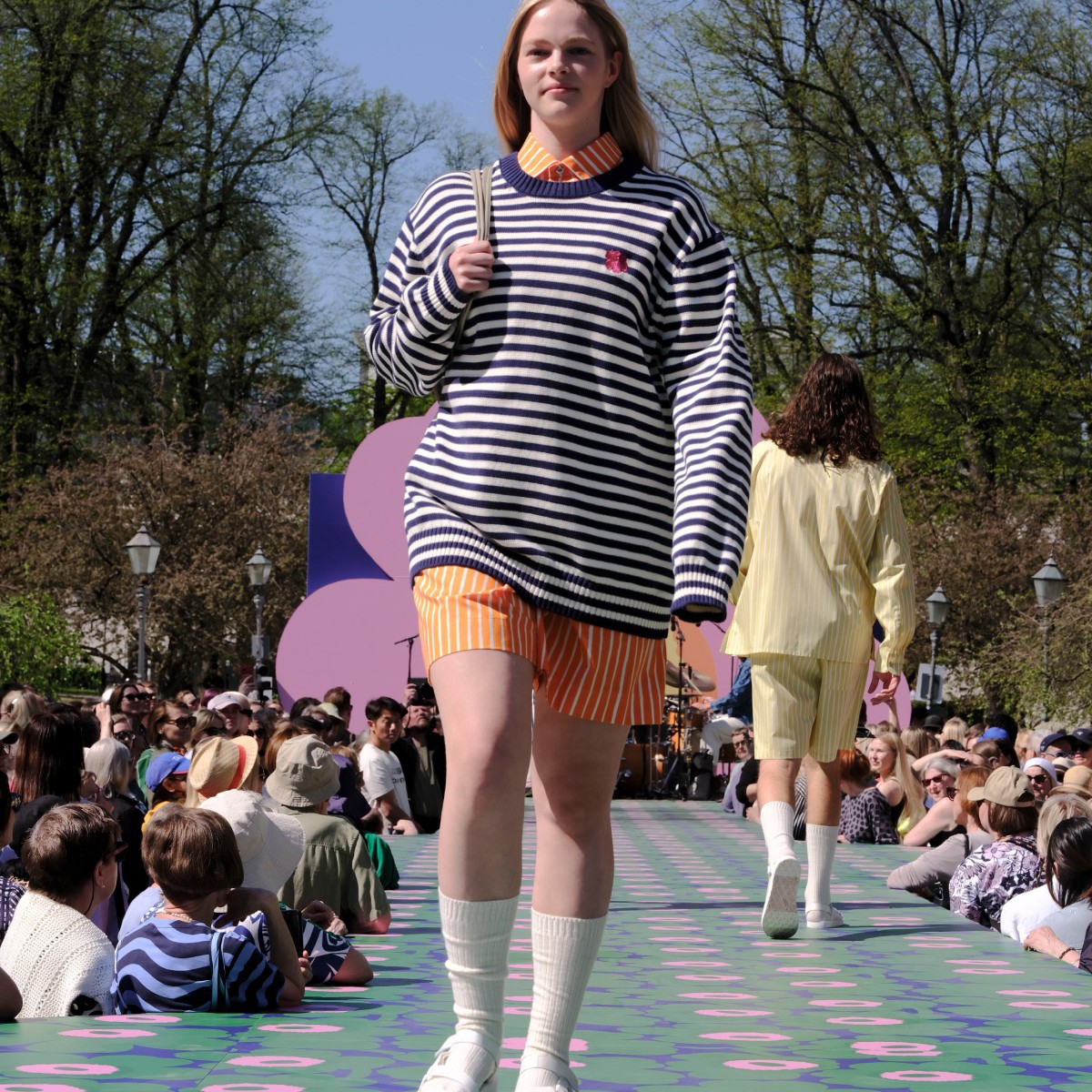 Model wearing blue and white tasaraita knit, orange Jokapoika shirt and orange Jokapoika shorts.