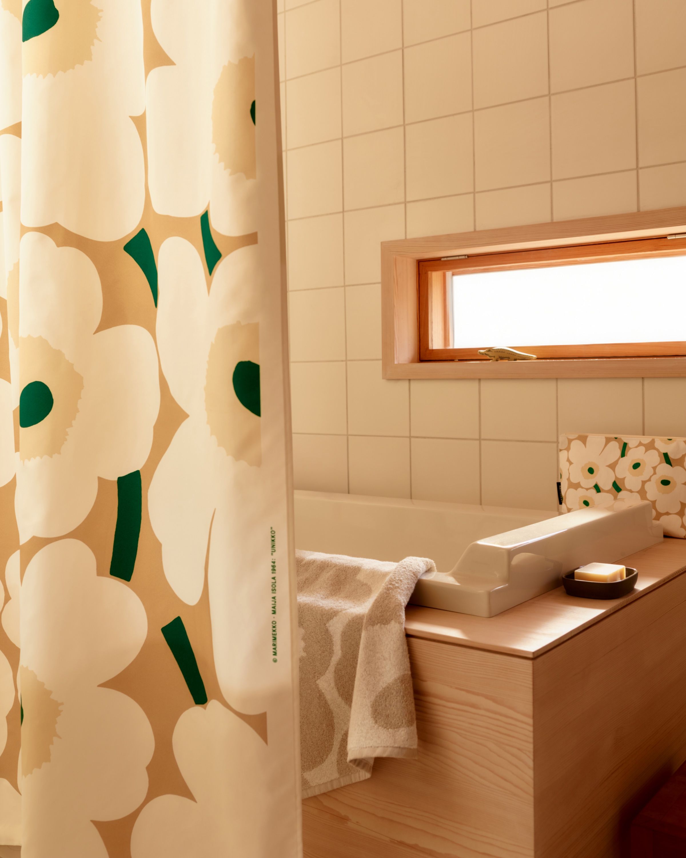 Unikko-printed towel and cosmetic bag on a bathtub, with a matching shower curtain beside it..