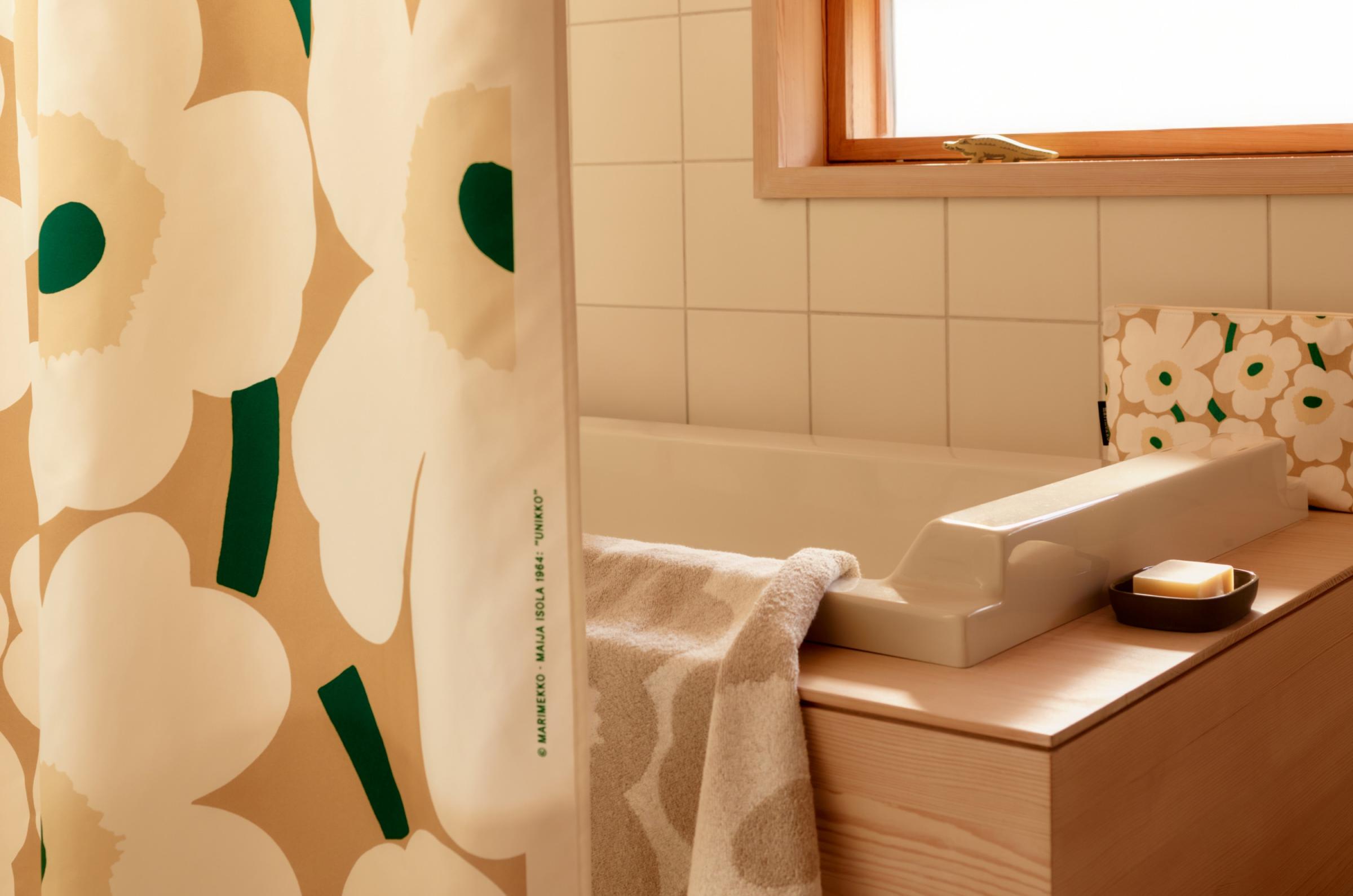 Unikko-printed towel and cosmetic bag on a bathtub, with a matching shower curtain beside it..