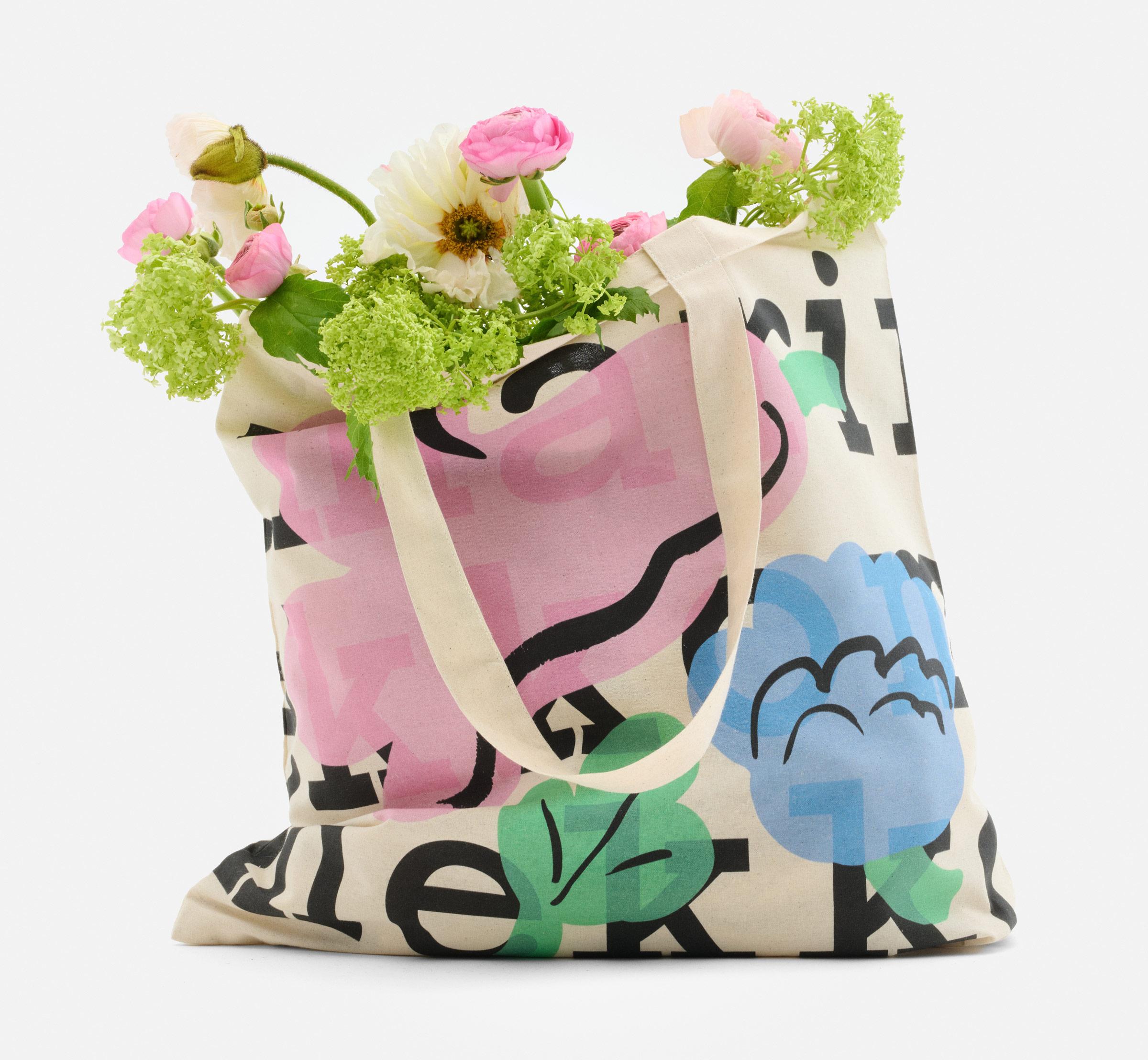 Logo tote, with a logo text and Kukasta kukkaan print, filled with flowers.