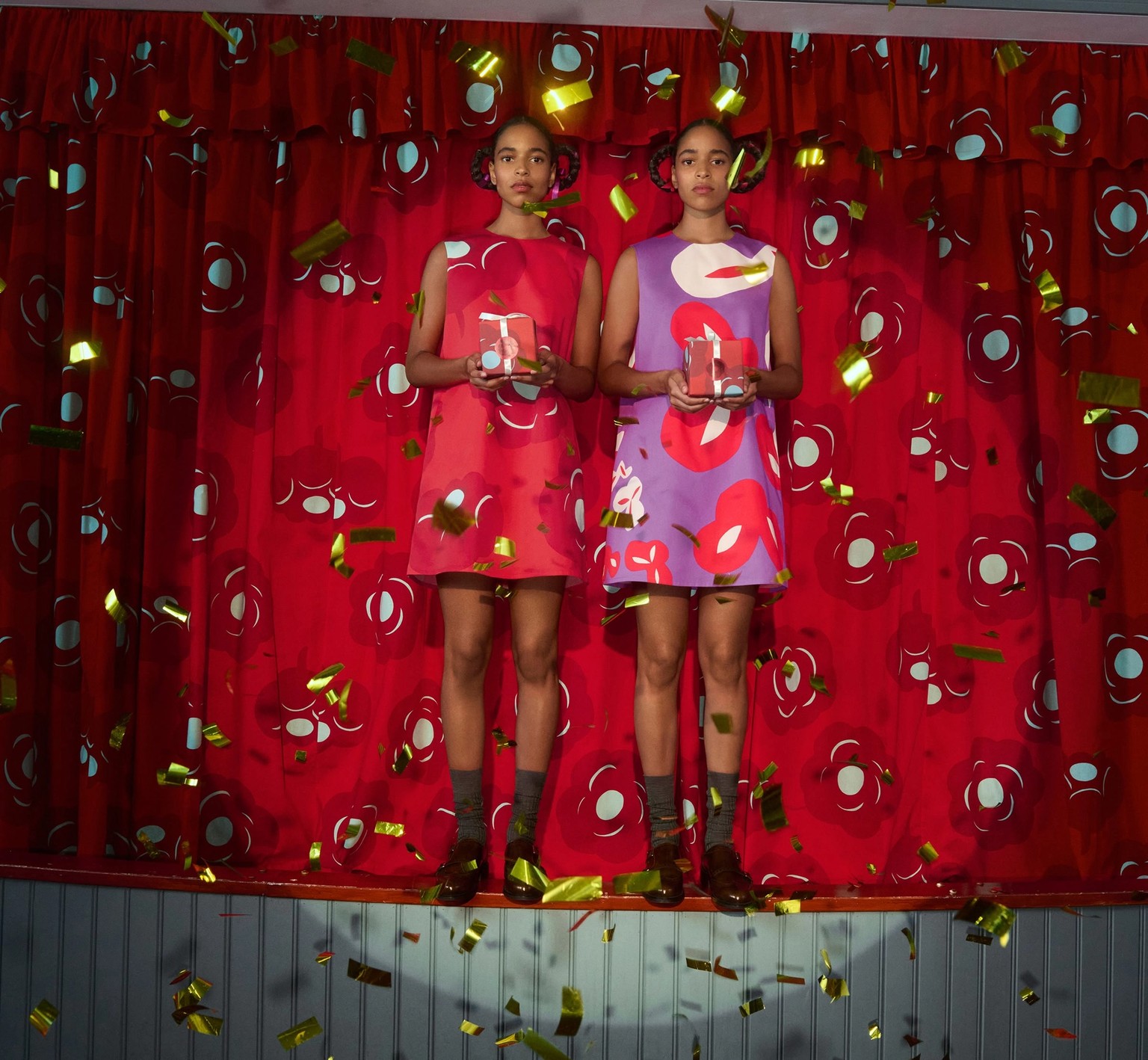 Kaksoset seisovat lavalla mekoissa ja jakavat lahjoja.