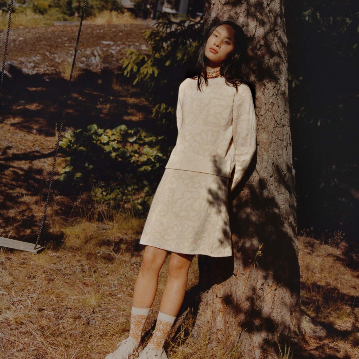 Model wearing beige Uniqlo and Marimekko collaboration shirt, dress and socks in sunny forest