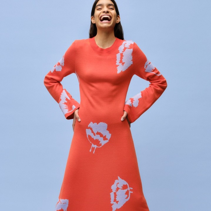 A smiling model dressed in a red Myski patterned knitted dress.