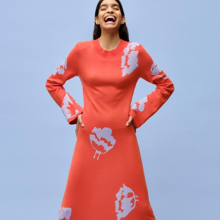 A smiling model dressed in a red Myski patterned knitted dress.