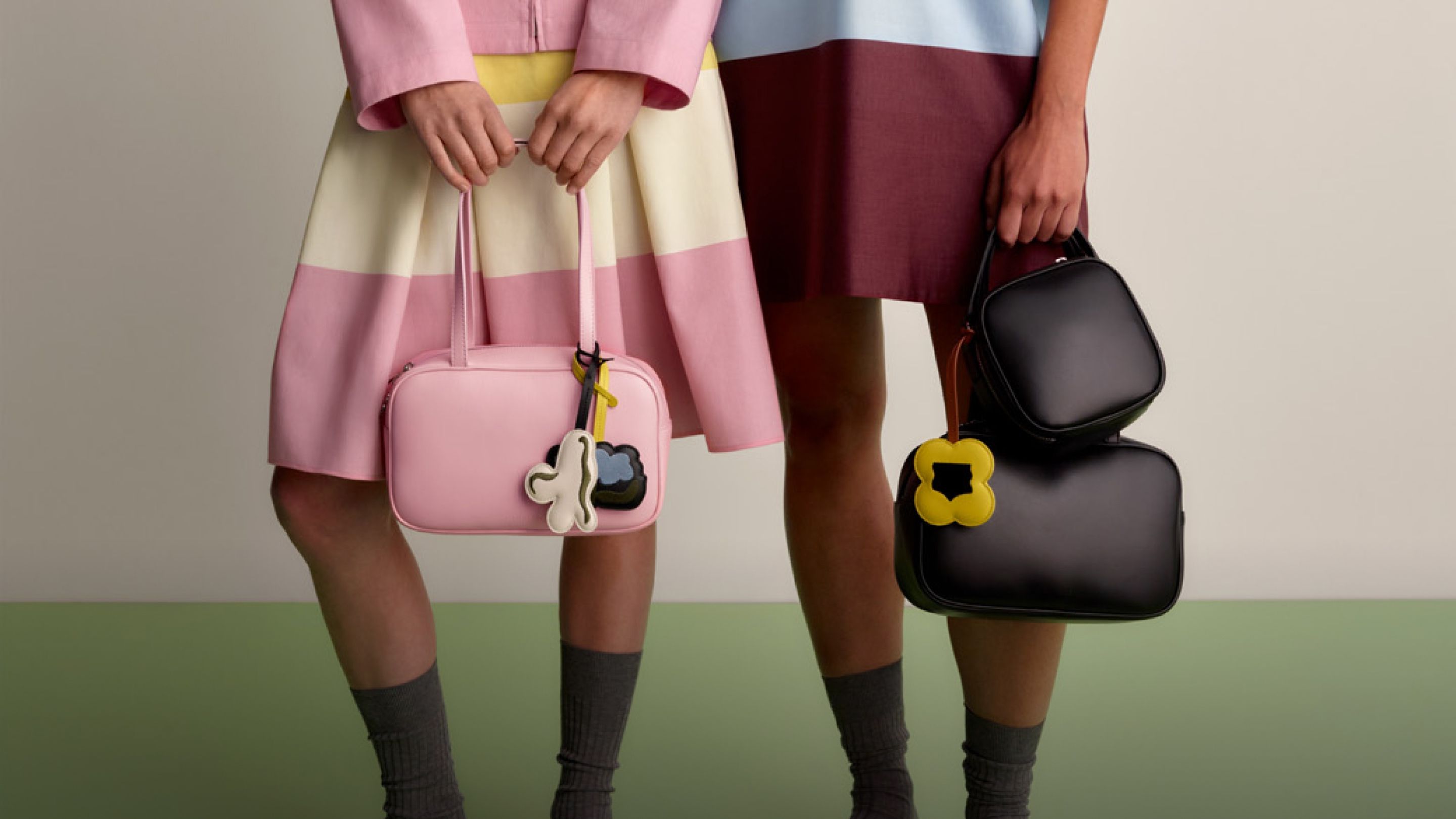 One model wearing a collar shirt and matching skirt in Hennika print, and another model wearing a sleeveless Hennika dress in darker colors. Both models carry Gratha leather bags in two different sizes and colors.