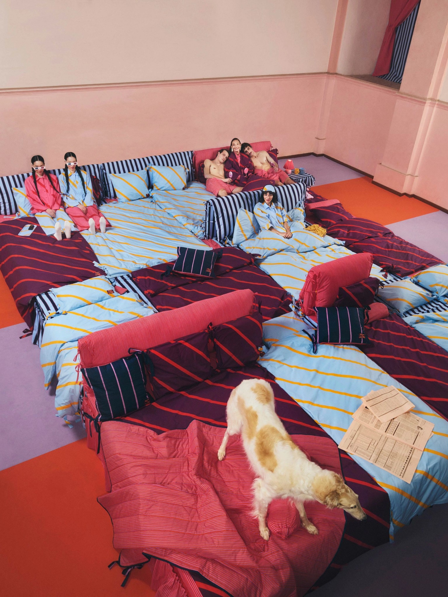 Models sitting on a big bed wearing Laila Gohar x Marimekko collection items.