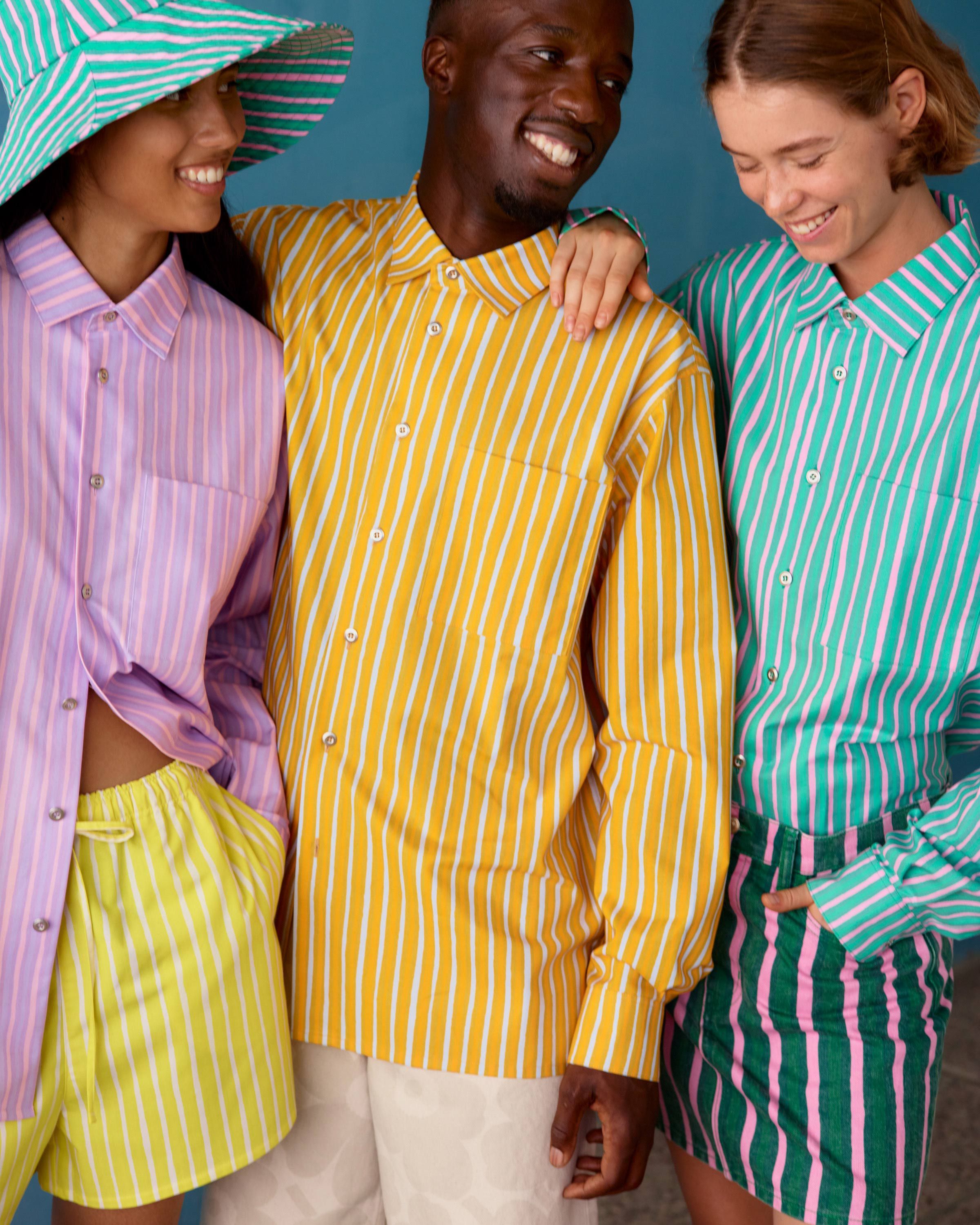 Three models wearing Jokapoika shirts in pink, yellow and blue Piccolo prints. 