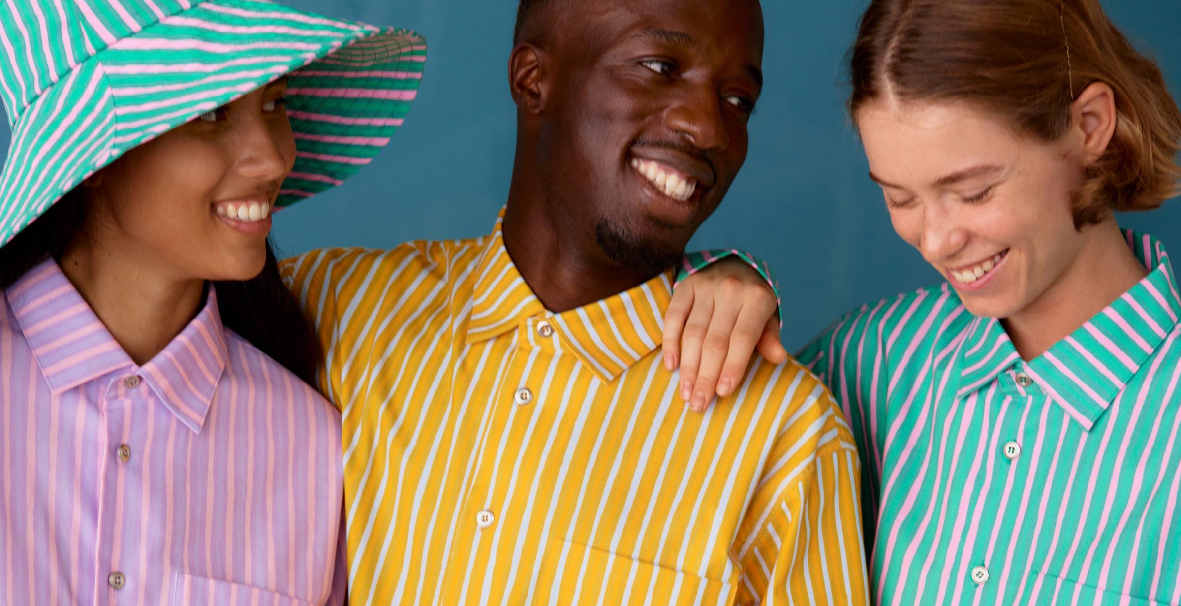 Three models wearing Jokapoika shirts in pink, yellow and blue Piccolo prints.