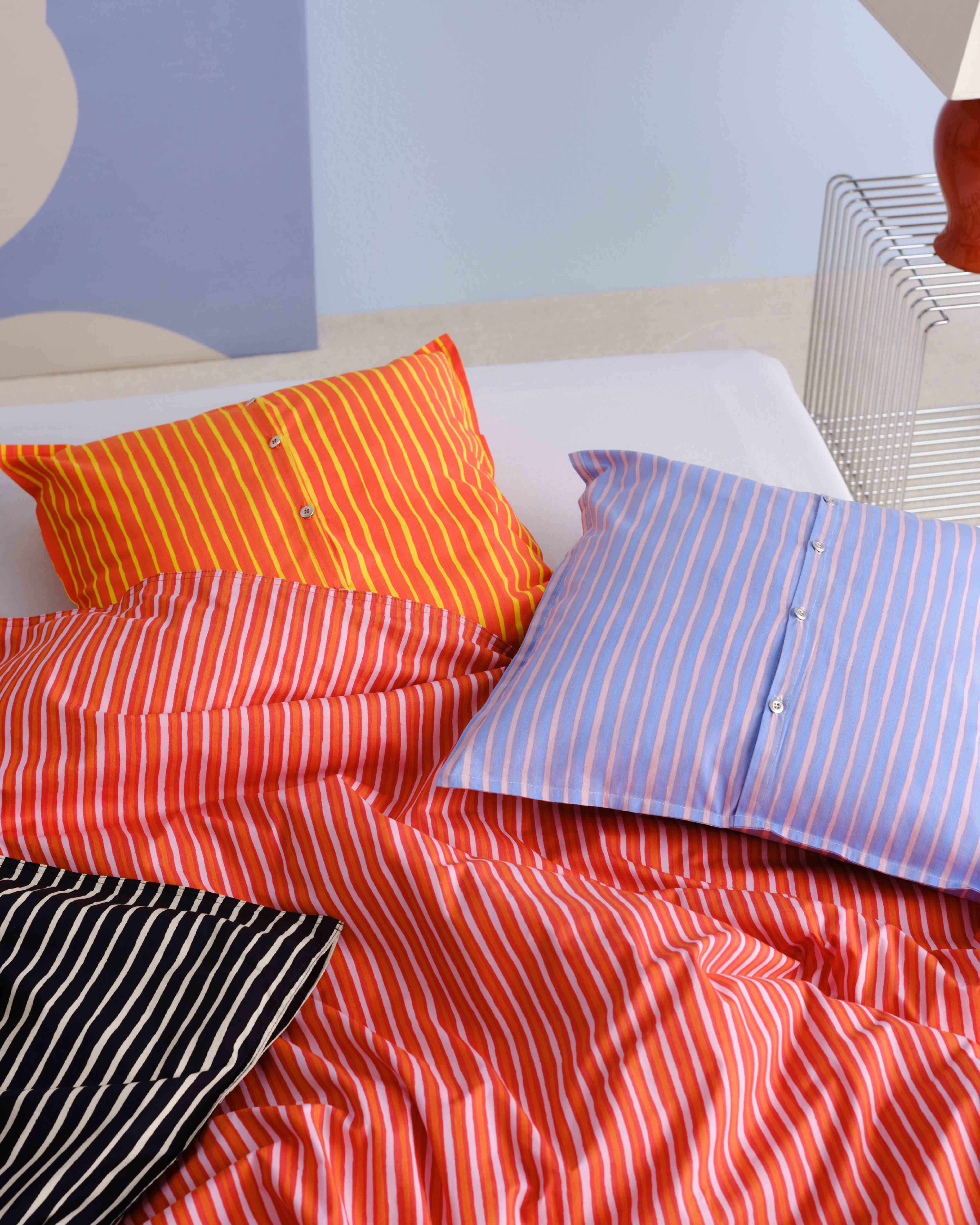Bed covered with red, orange, and lilac Piccolo print duvet and cushion covers