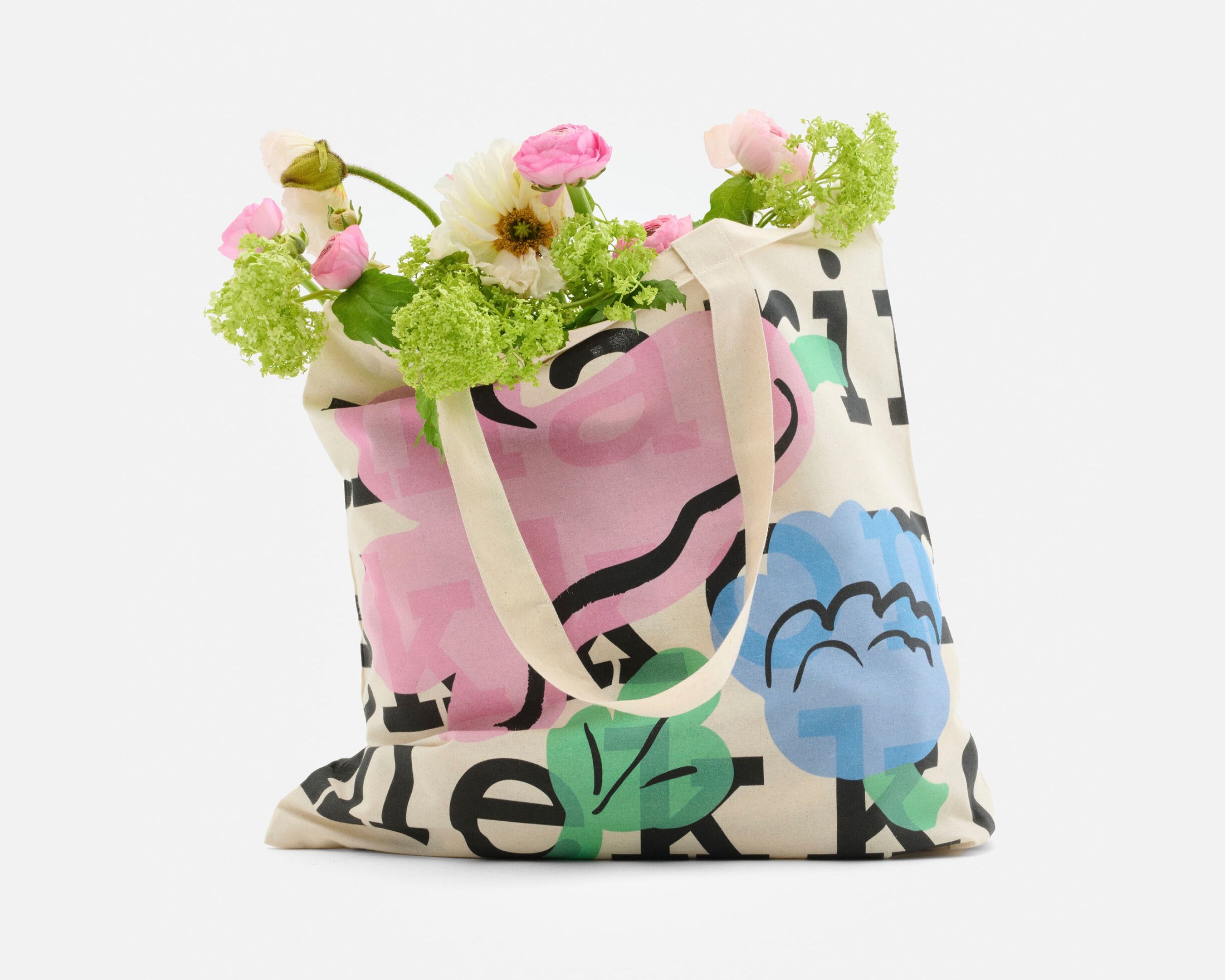 Logo tote, with a logo text and Kukasta kukkaan print, filled with flowers.