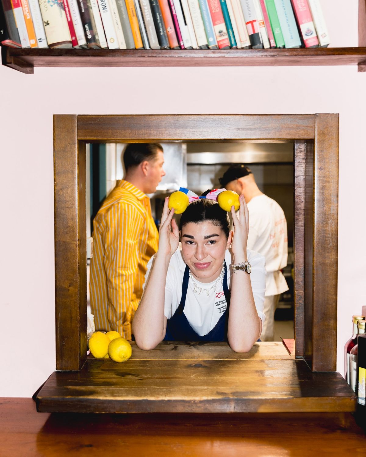 A person posing in a window with lemons on her head.