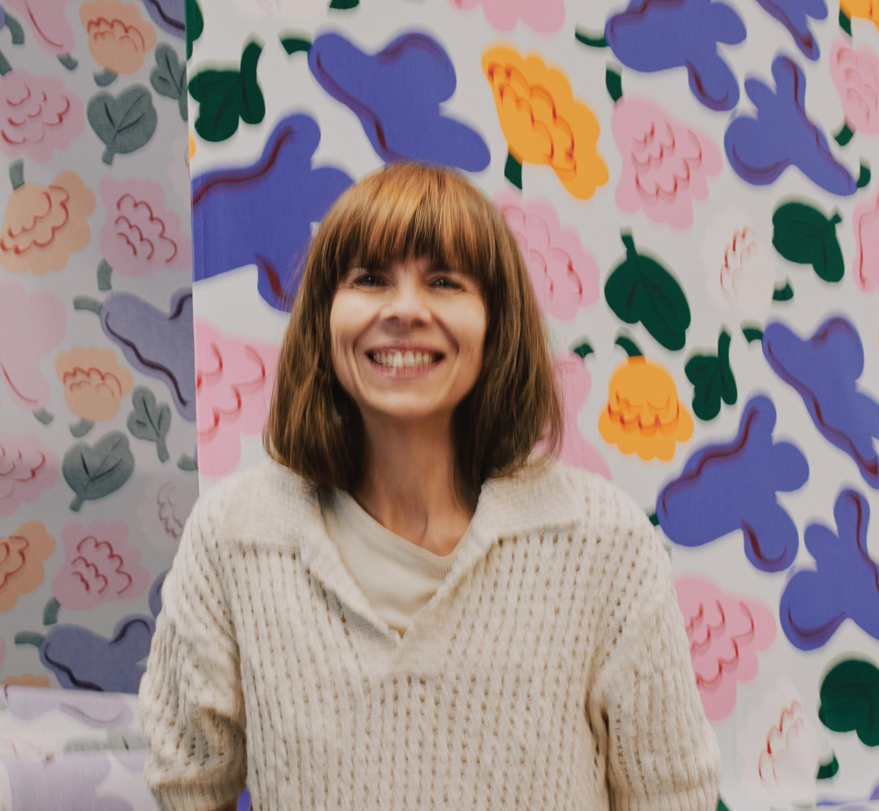 Portrait of Erja Hirvi infront of Kukasta kukkaan print.