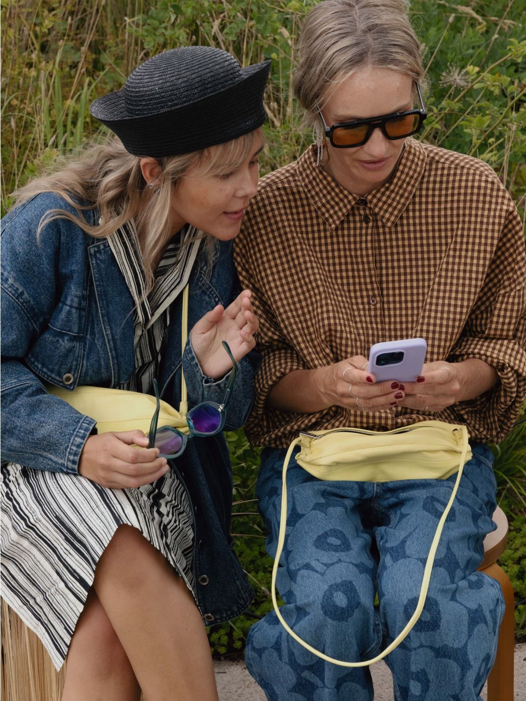 Sofie Ken and Hanni Gohr sitting and browsing phone together. They have matching light yellow Karla bags.