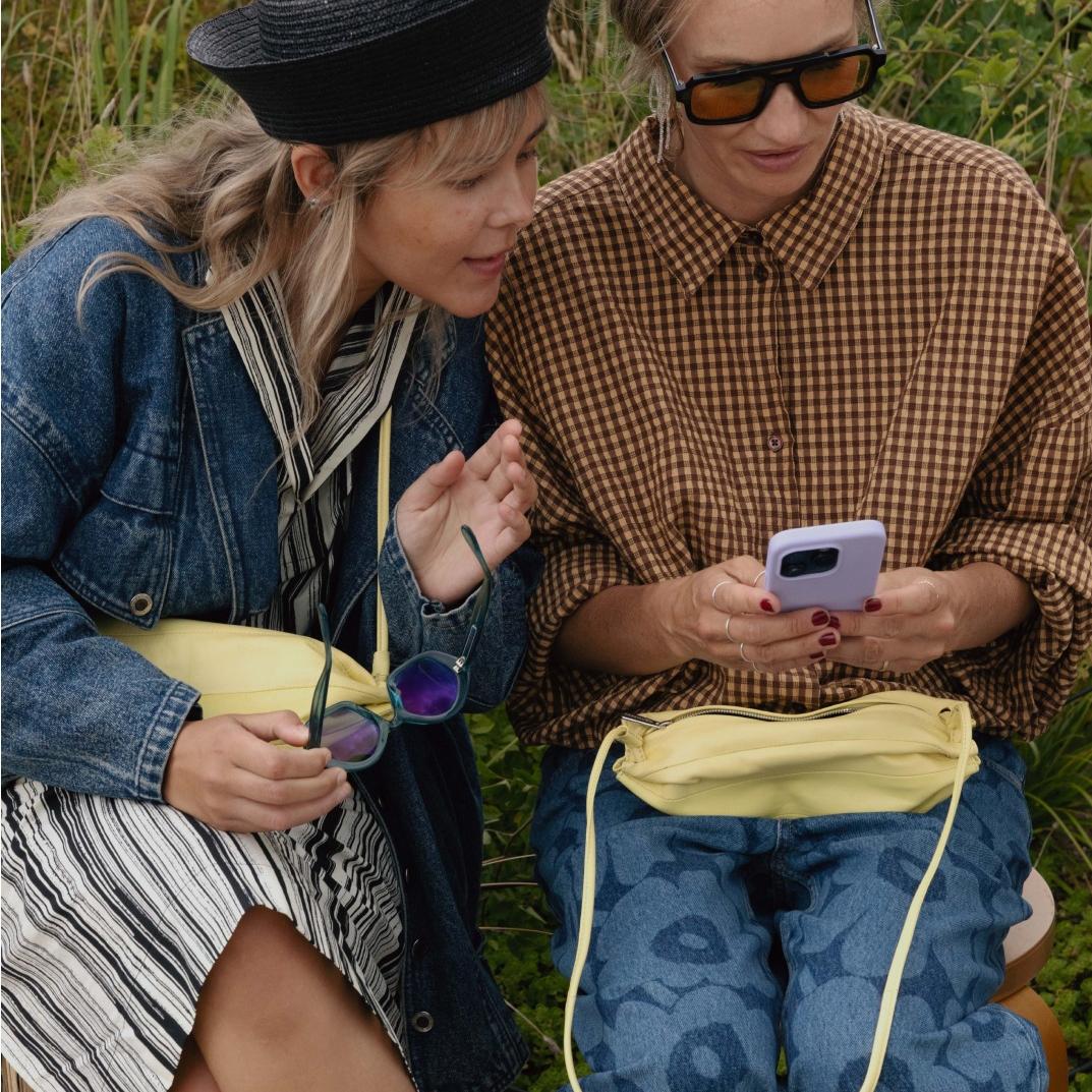 Sofie Ken and Hanni Gohr sitting and browsing phone together. They have matching light yellow Karla bags.