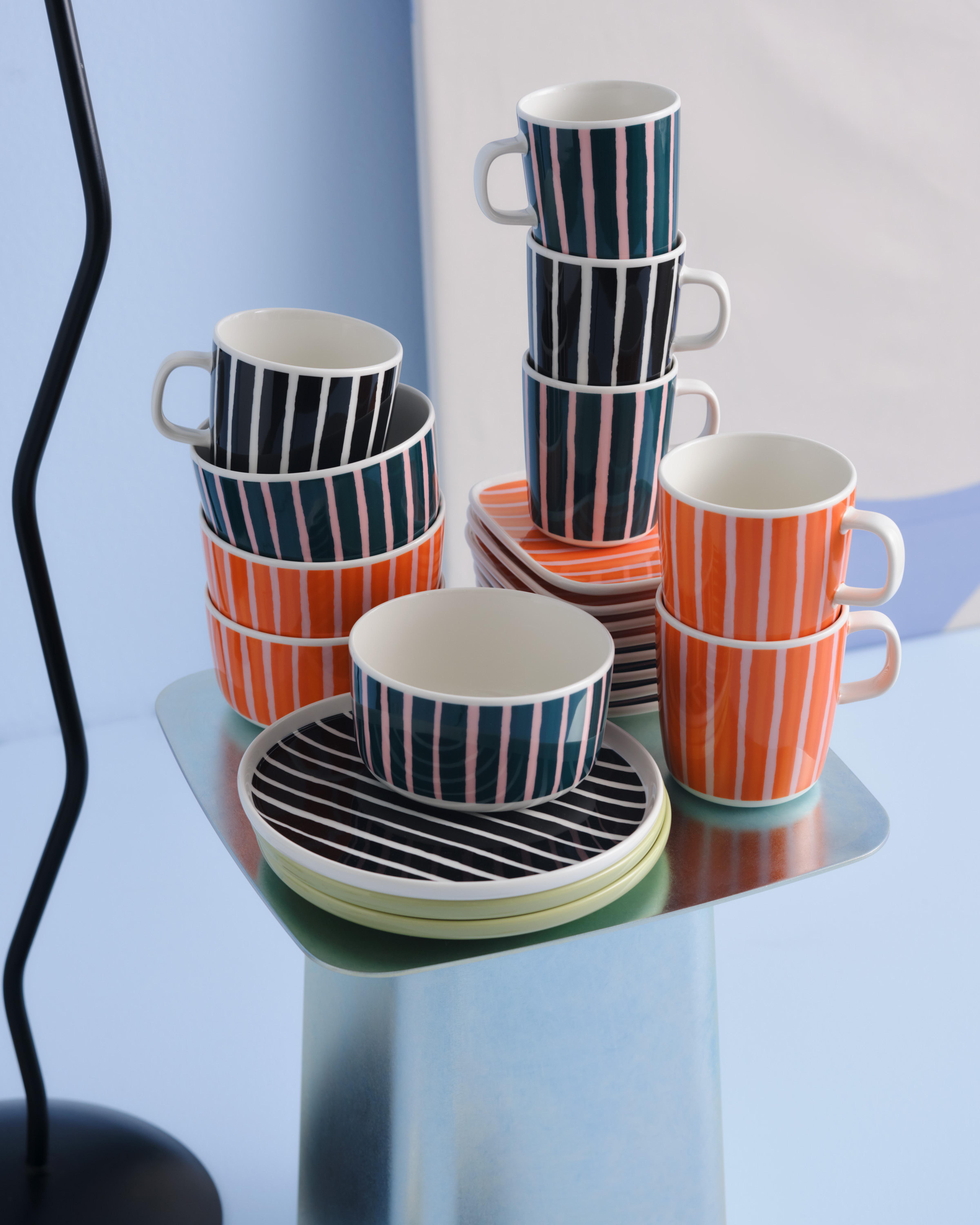 Stacks of Piccolo print plates, bowls, and mugs in orange, black and white, and green and pink colorways