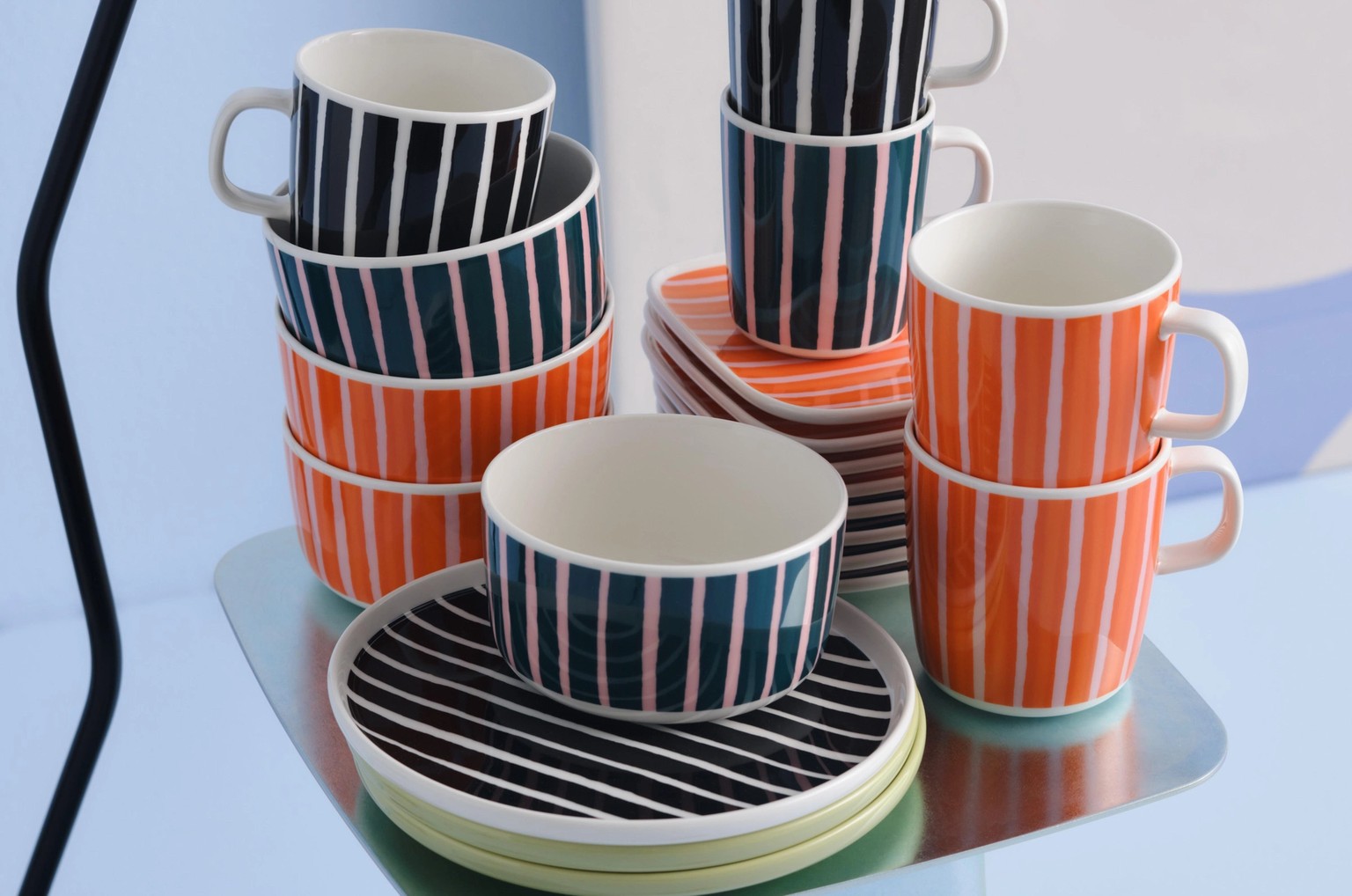 Stacks of Piccolo print plates, bowls, and mugs in orange, black and white, and green and pink colorways