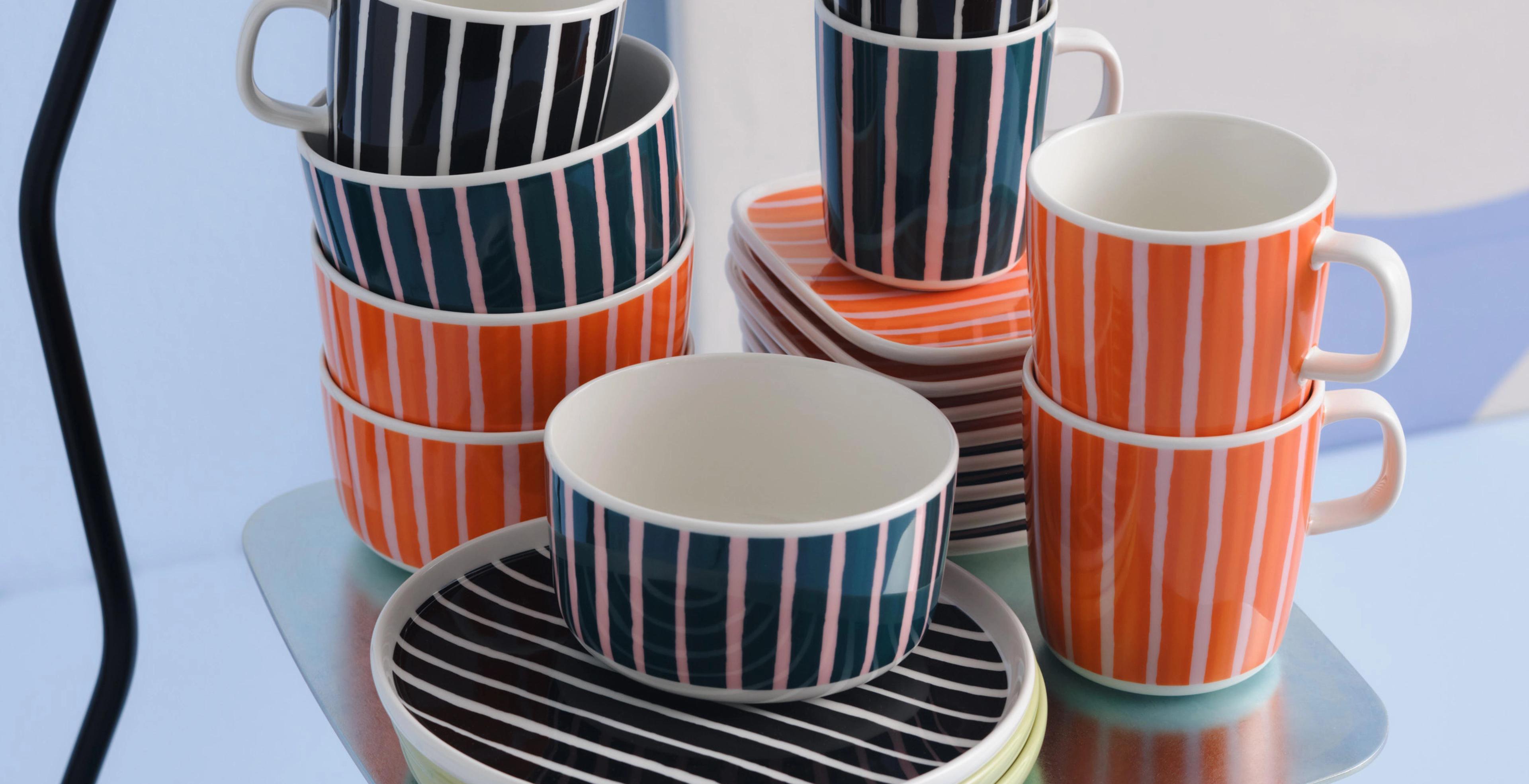 Stacks of Piccolo print plates, bowls, and mugs in orange, black and white, and green and pink colorways