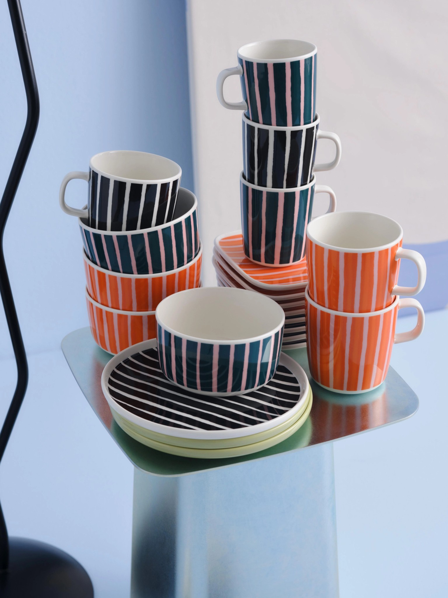 Stacks of Piccolo print plates, bowls, and mugs in orange, black and white, and green and pink colorways