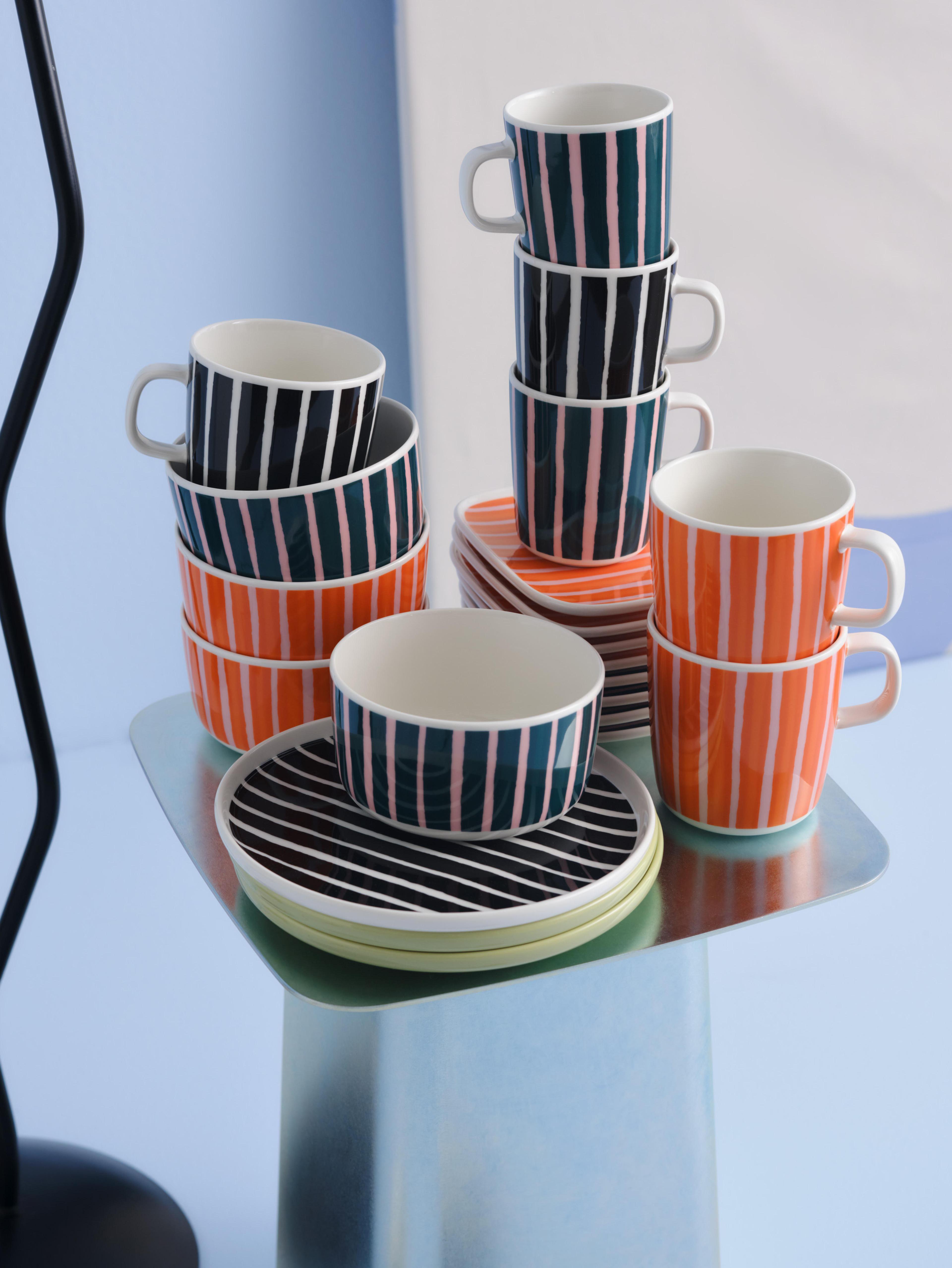 Stacks of Piccolo print plates, bowls, and mugs in orange, black and white, and green and pink colorways