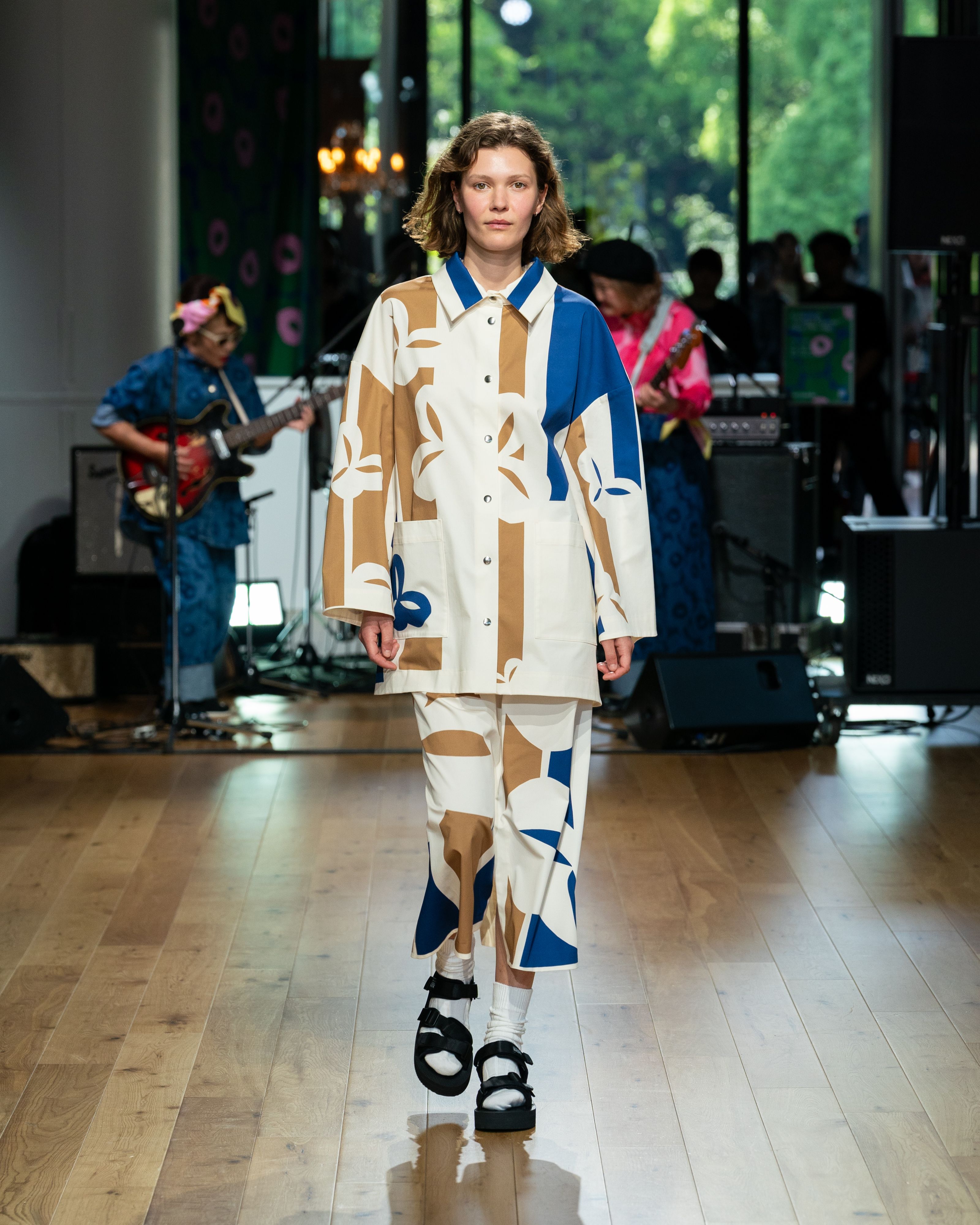 Model wearing white-beige-blue jacket and skirt. 