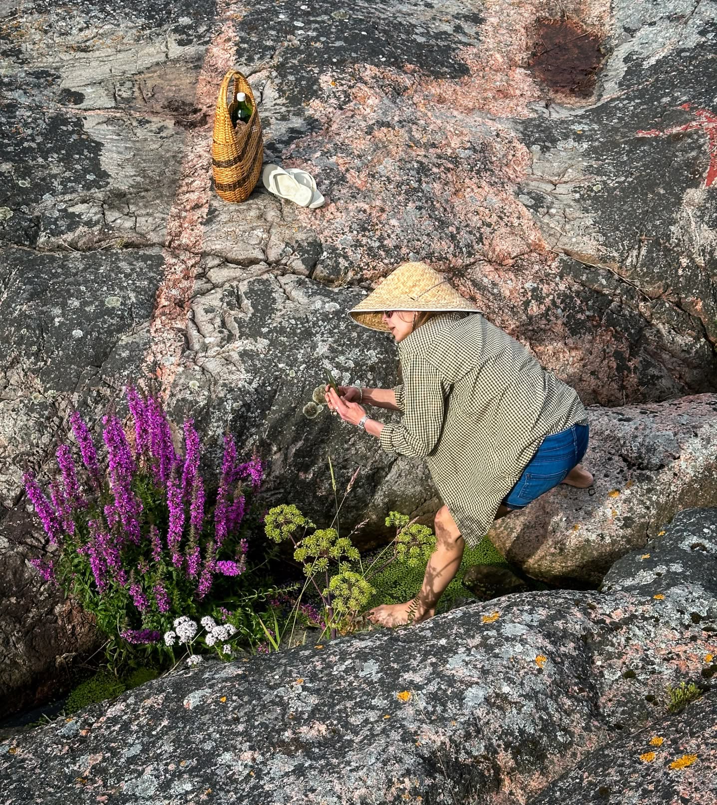 A woman inspecting flowers in a rock formation.
