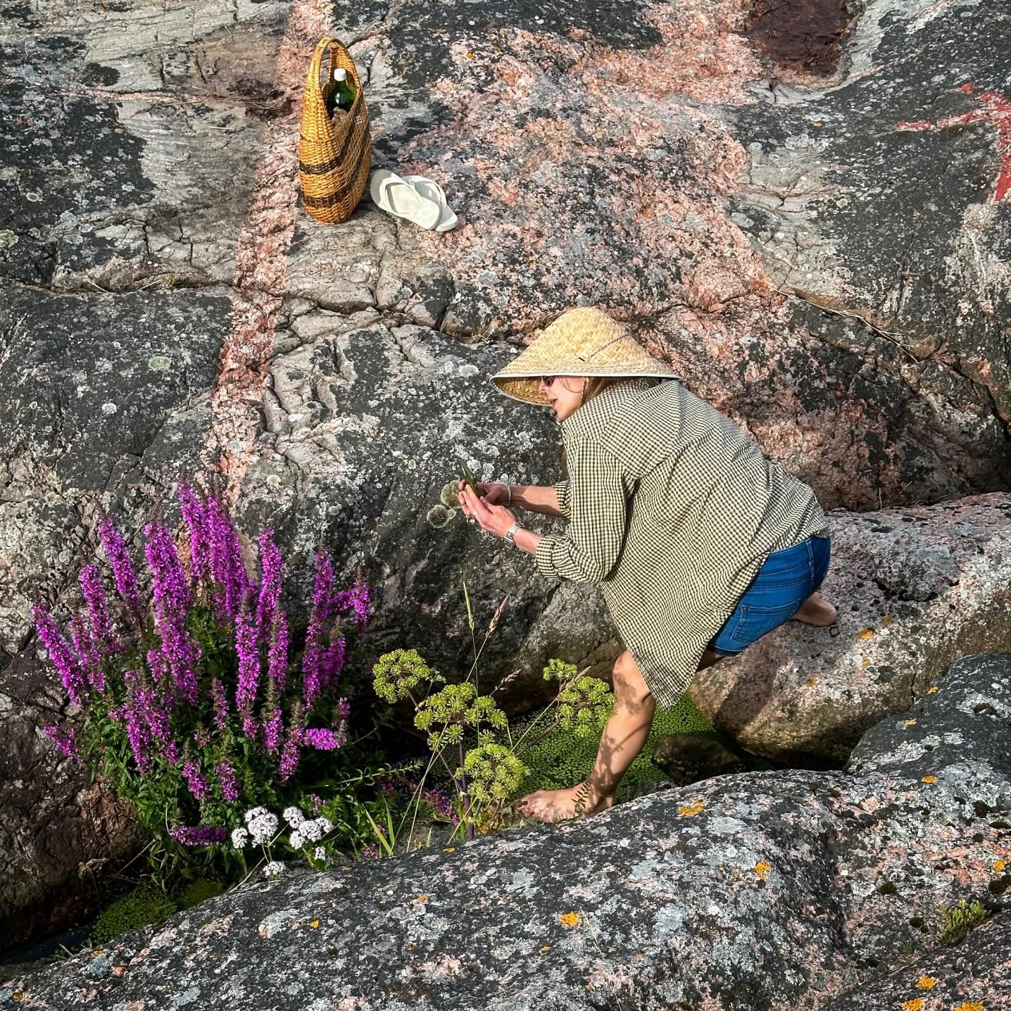 Une femme inspectant des fleurs dans une formation rocheuse.