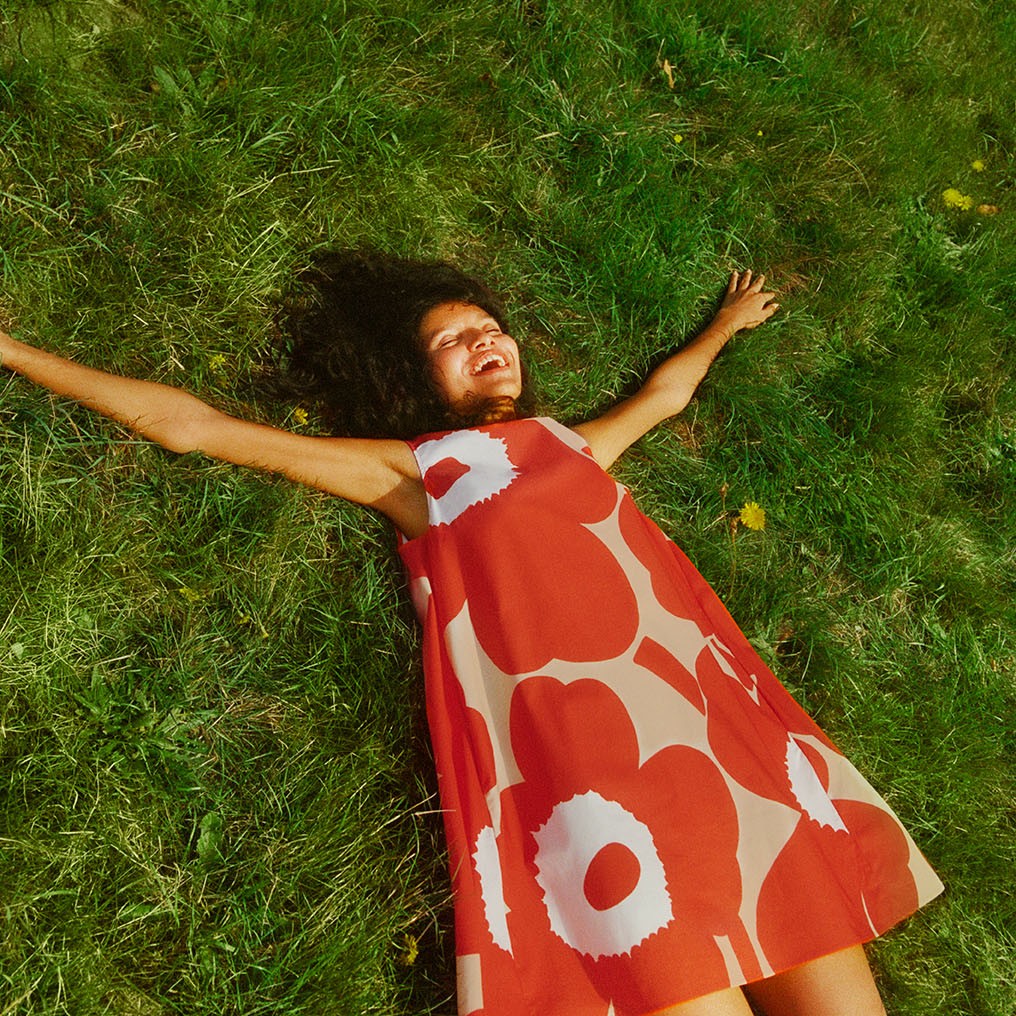 Model laying on the field wearing Marimini dress in Unikko pattern.