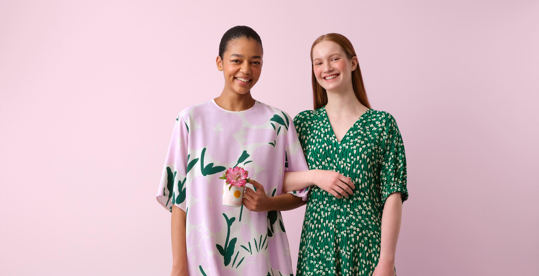 Mallien yllä mekot Tuulahdus- ja Talkoot-kuoseissa ja he pitelevät laukkuja, joissa on Marimerkki-kuosi. Maassa kaksi Auringonkukka-kuosi tyynyä.