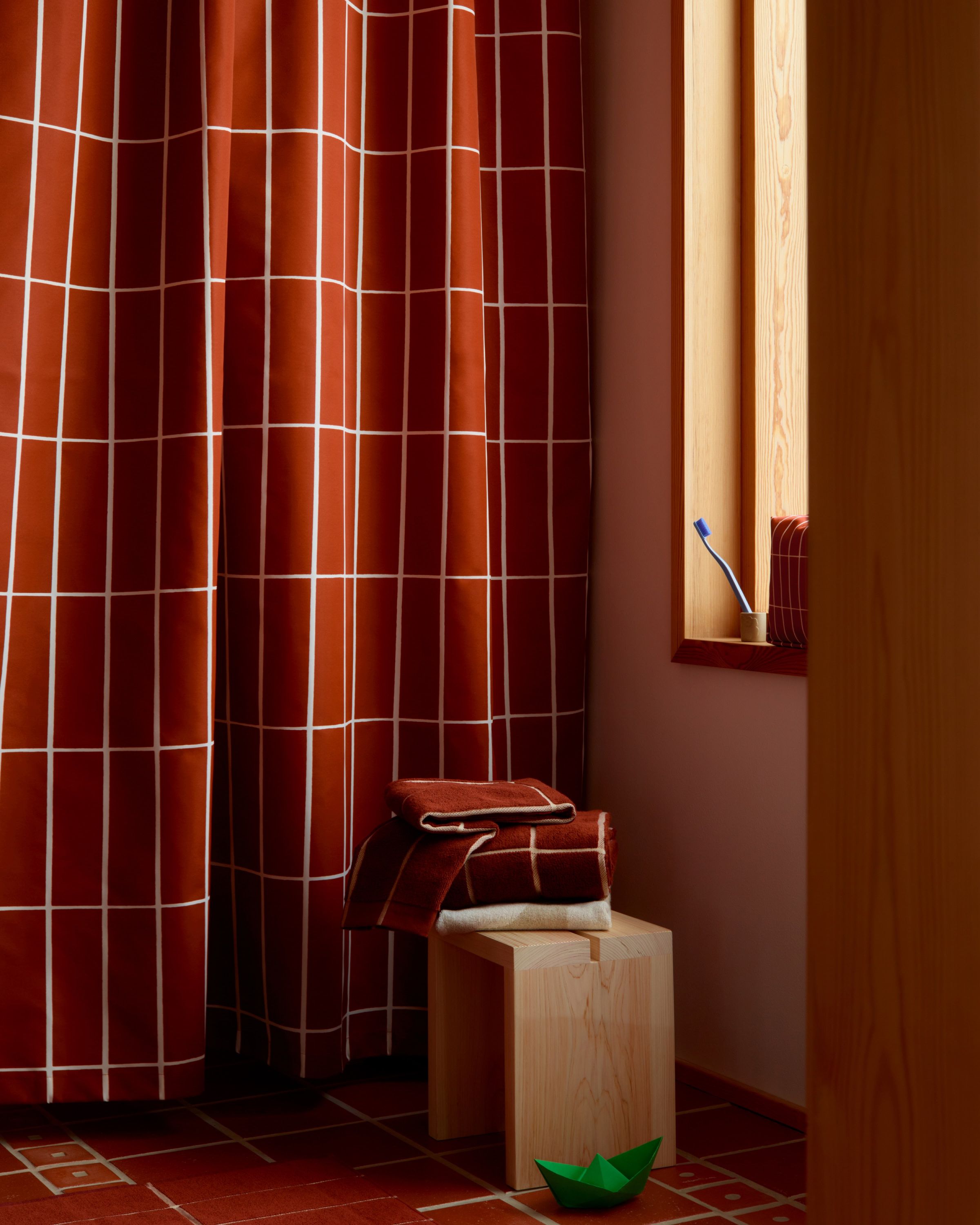 Matching shower curtain and towels in brick red Tiiliskivi print in a bathroom.