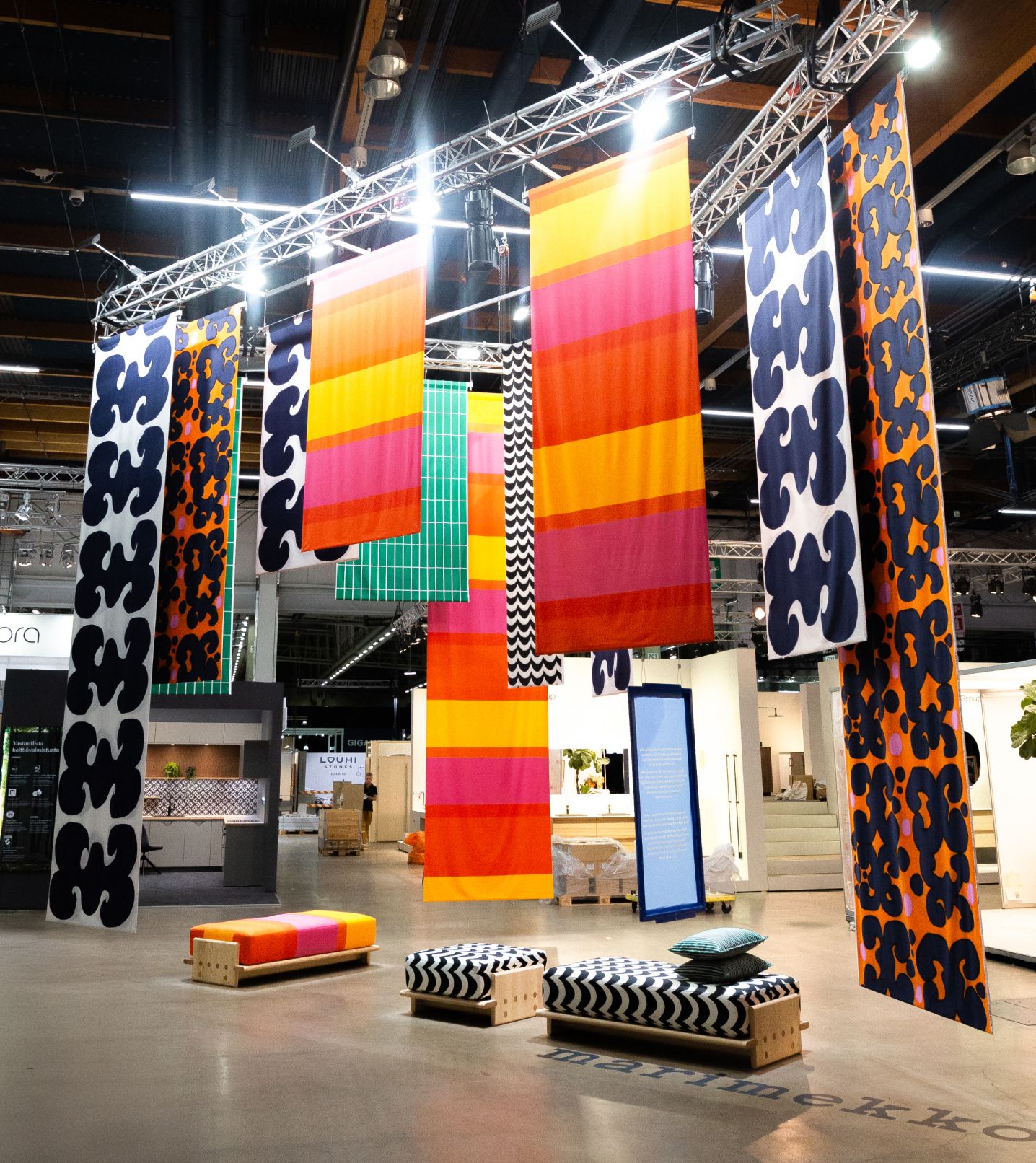 The entire installation at the Habitare fair, combining colorful patterned fabric hanging from the ceiling and wooden benches in Marimekko patterns.