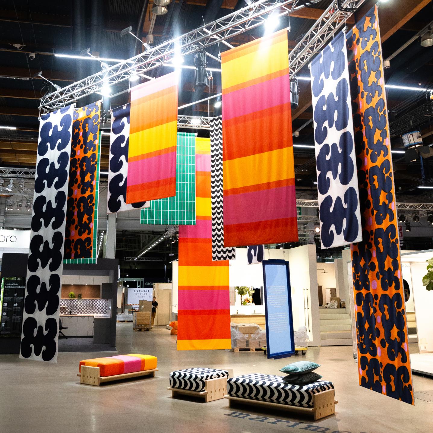 The entire installation at the Habitare fair, combining colorful patterned fabric hanging from the ceiling and wooden benches in Marimekko patterns.