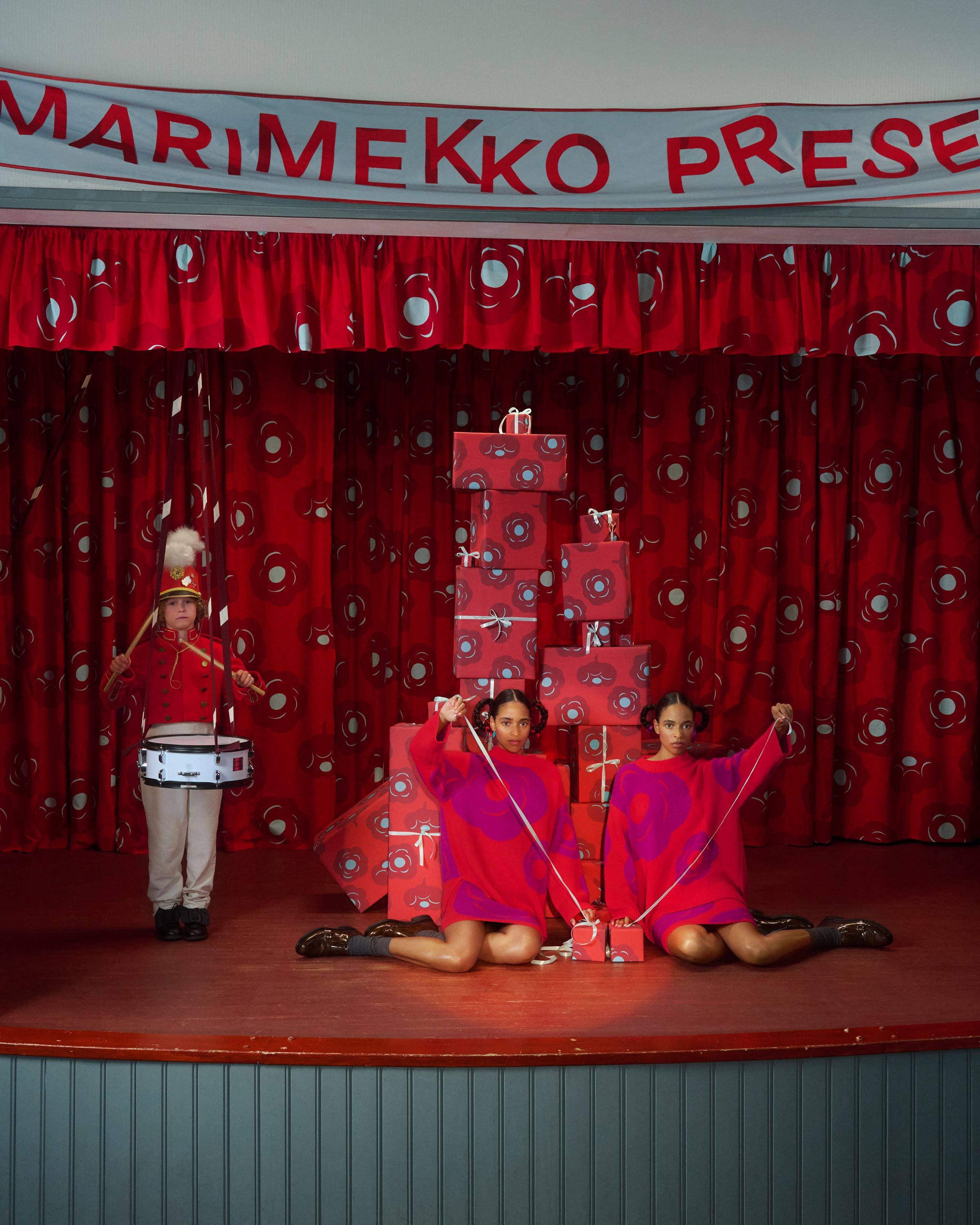 Two models sitting on a stage and a boy playing a drum.