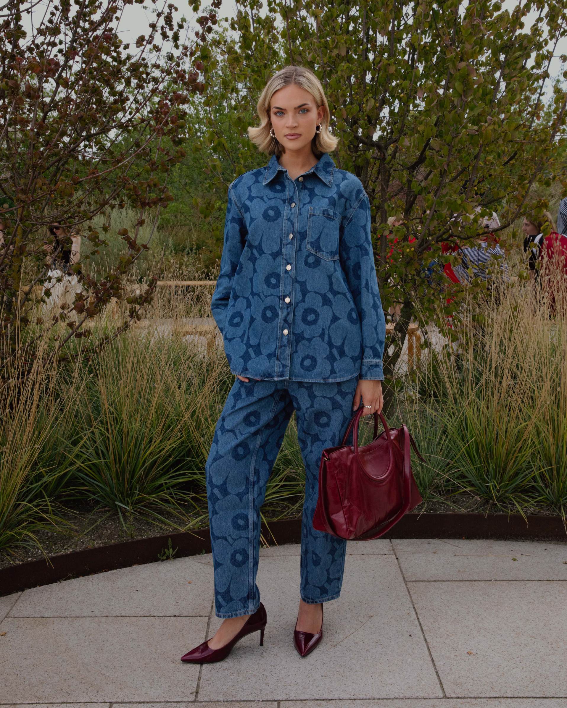 Emilia Silberg dressed in a Maridenim shirt and jeans, accompanied by a burgundy bag and high heels.