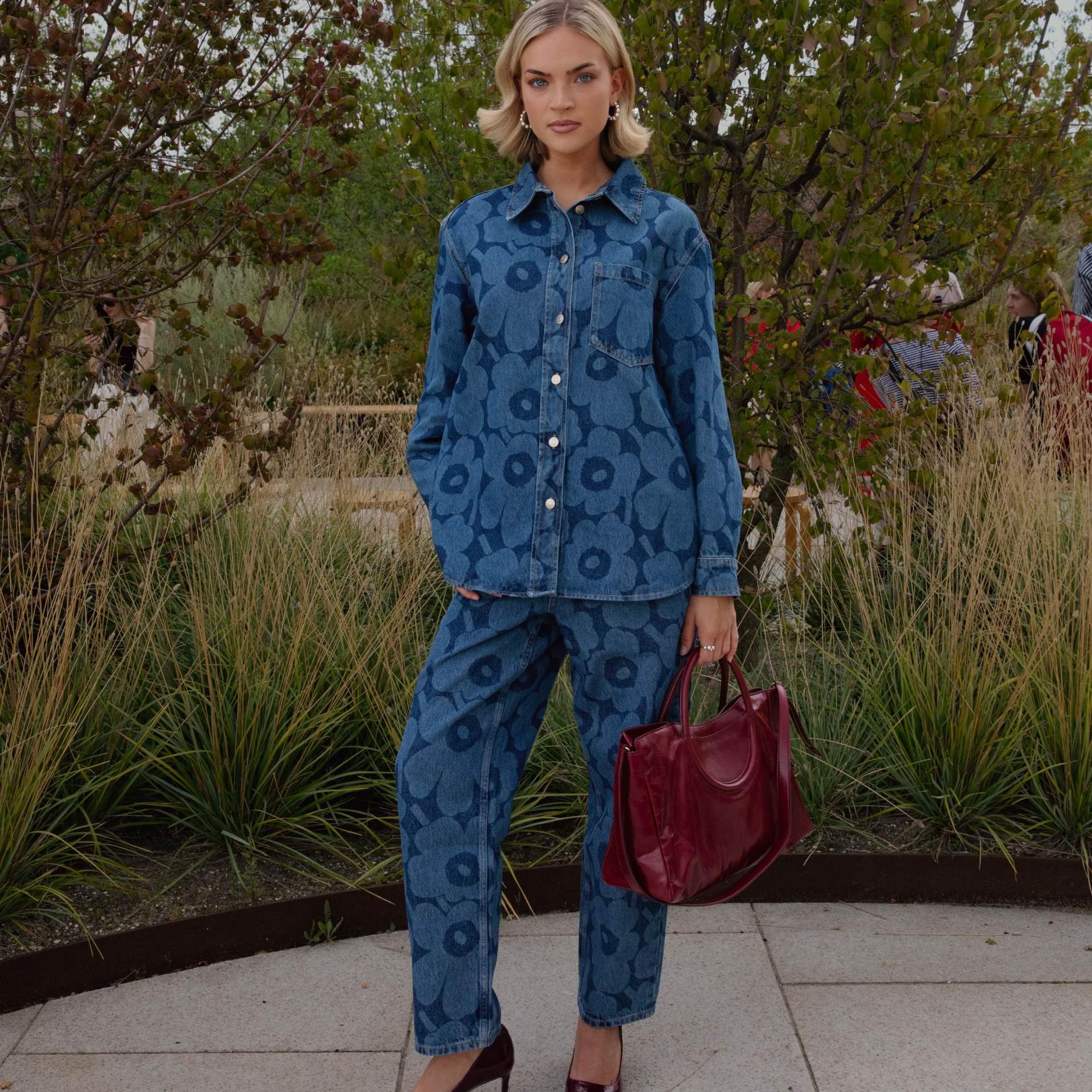 Emilia Silberg dressed in a Maridenim shirt and jeans, accompanied by a burgundy bag and high heels.