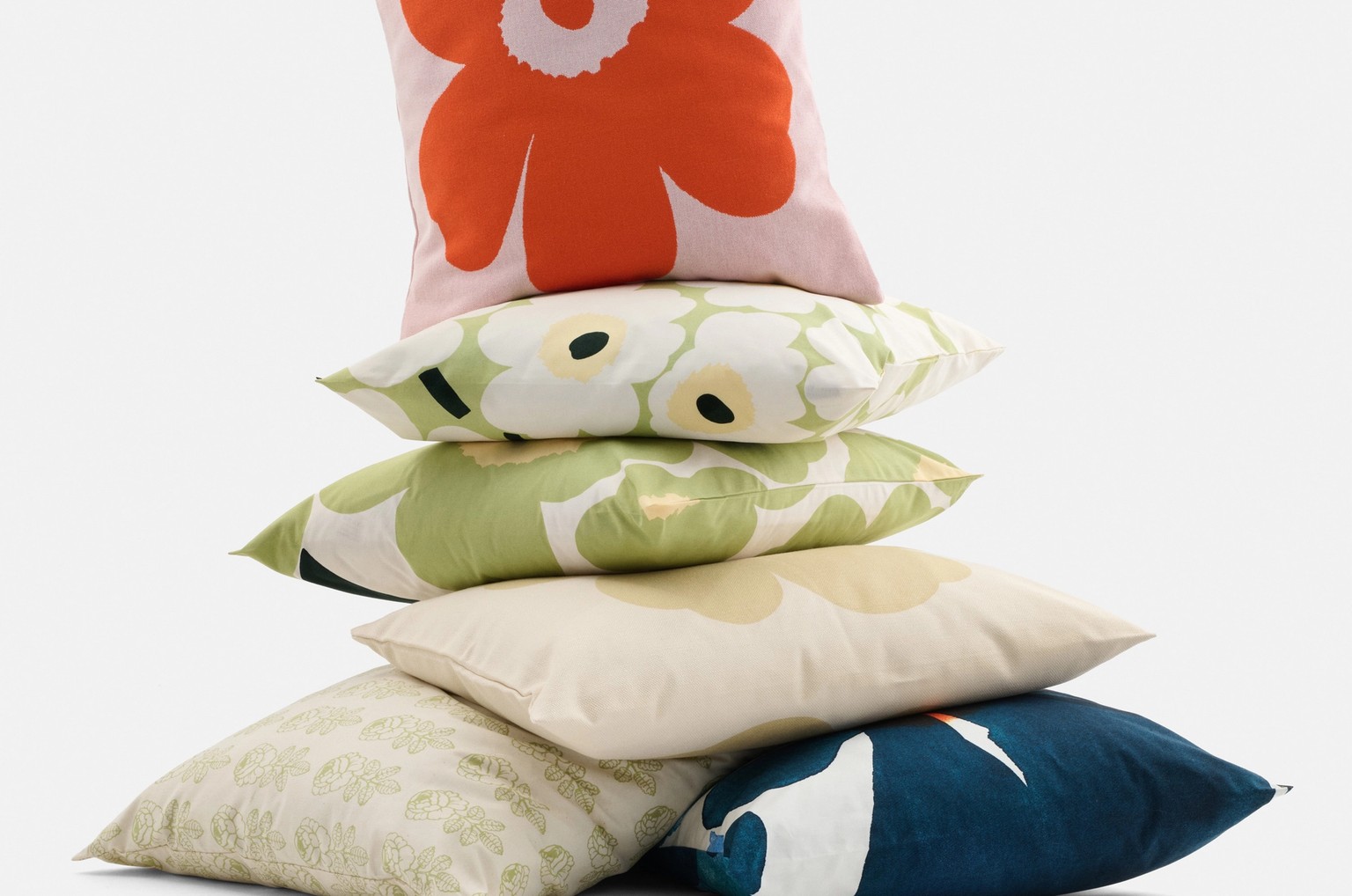 A pile of Unikko patterned pillows in different shades of red, pink, green, beige and blue.