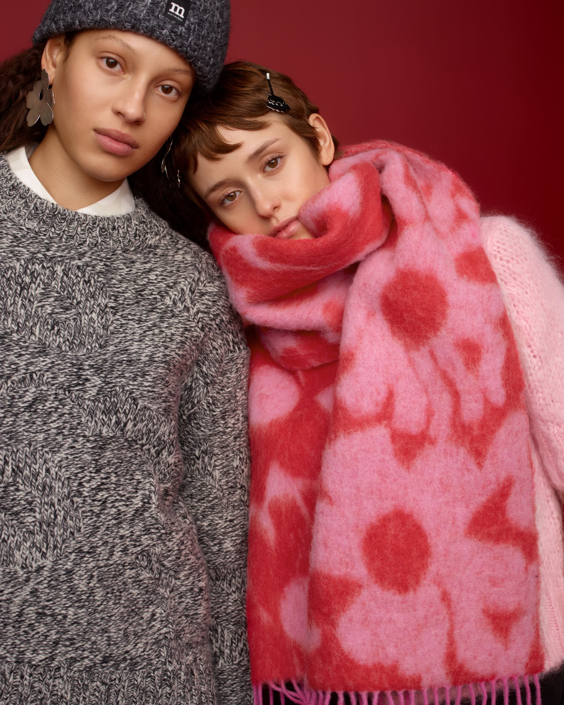 One model wearing a grey sweater and a grey beanie with Marimekko logo, and the other wearing a red and pink scarf in Lossi print.