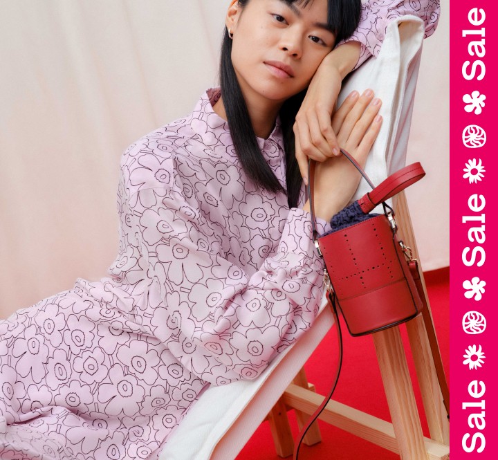 woman leaning on chair wearing pink unikko shirt and skirt holding a red leather bucket bag