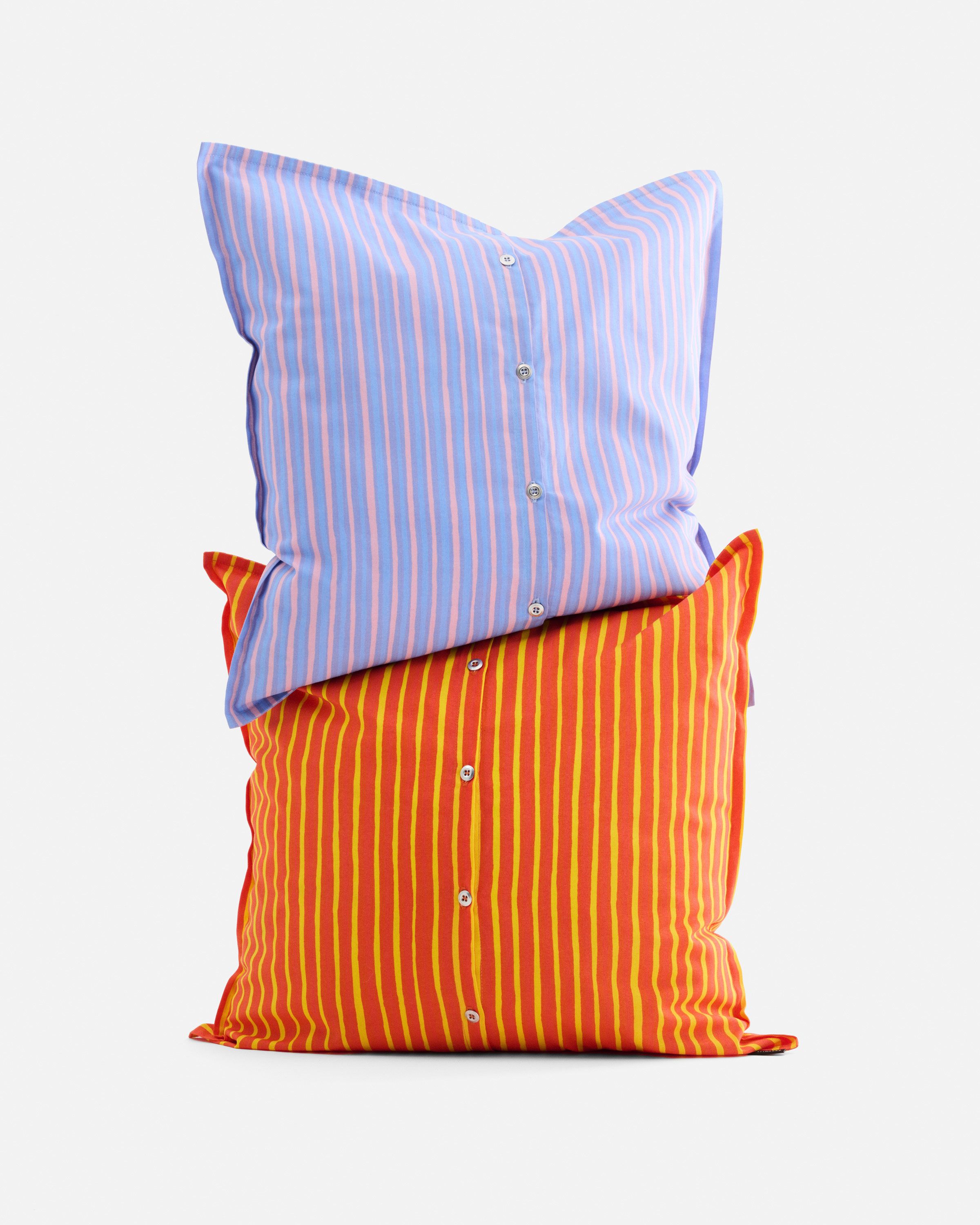 Oranssit ja vaalean liilat tyynyt napeilla Piccolo-kuosissa.