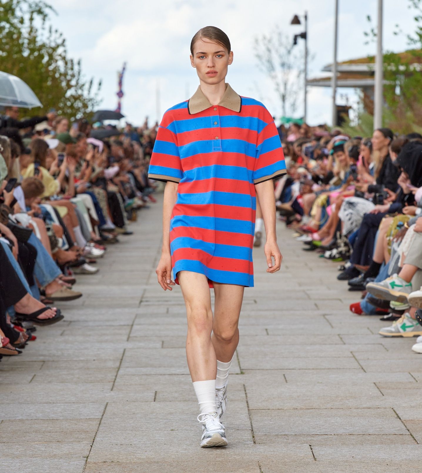 Model walking on the catwalk of the fashion show dressed in a blue-red Reference tunic.